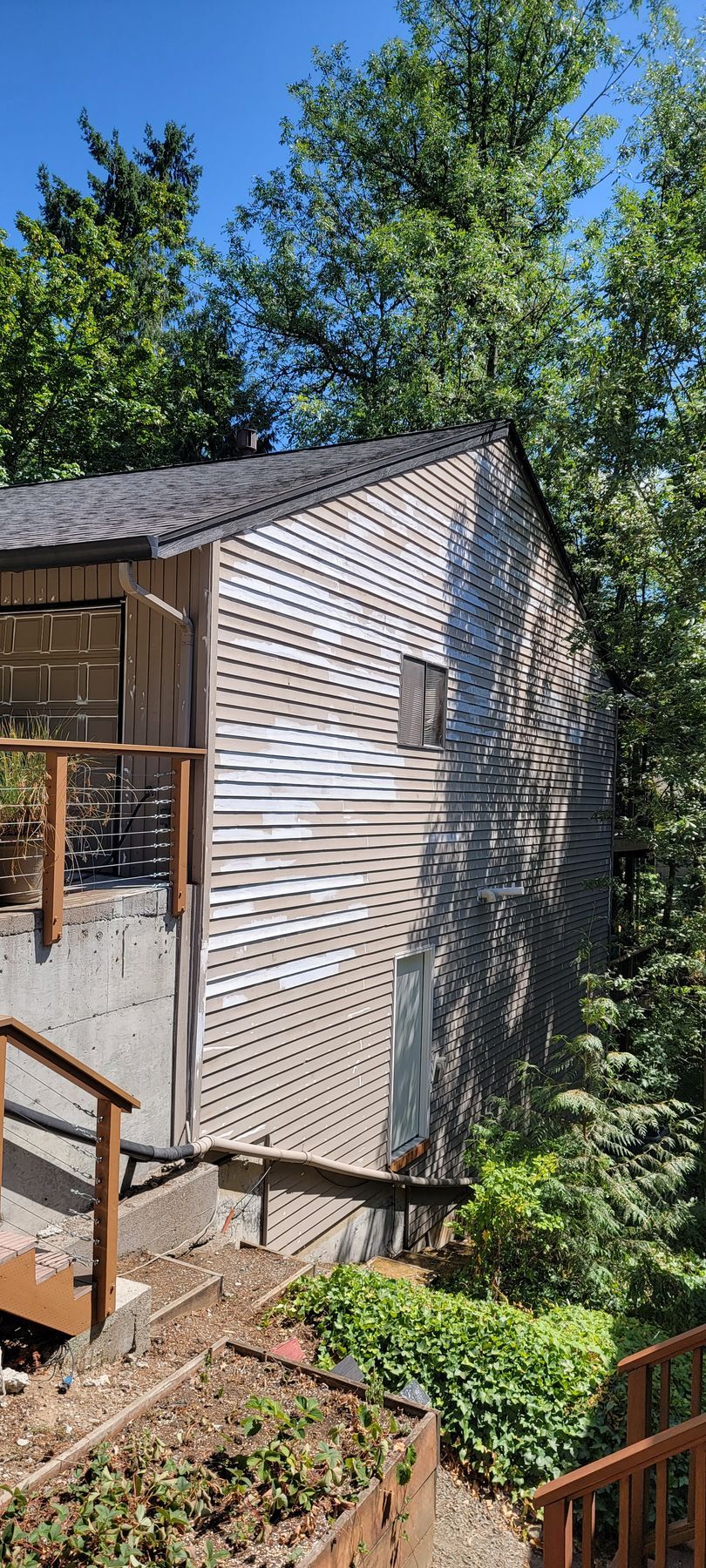 Side view of a weathered wooden house with a shingle roof nestled amongst trees and a clear blue sky.