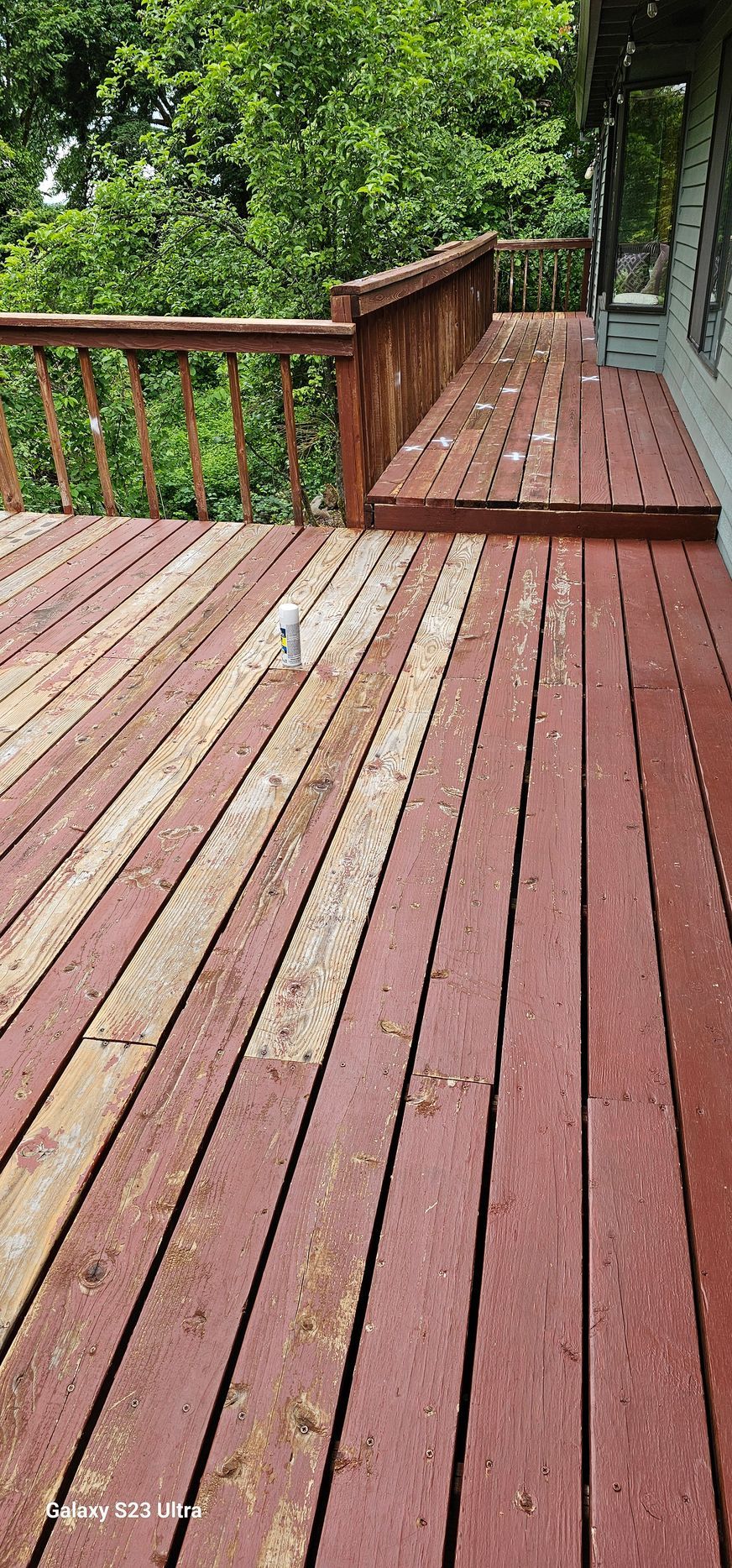 Wooden deck stained red, with a railing and surrounded by trees.