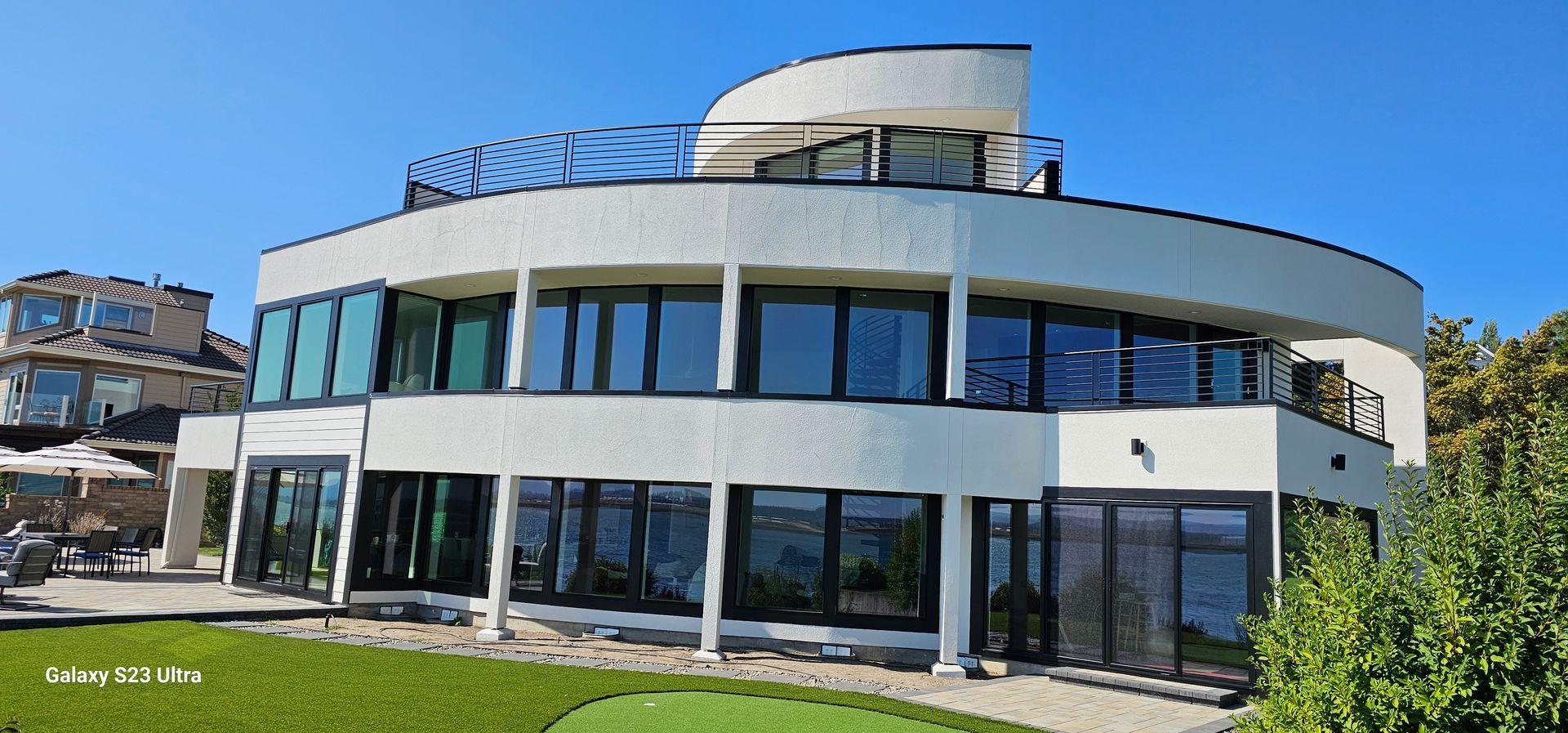 Modern, white building with large windows, curved design, green lawn, and blue sky.