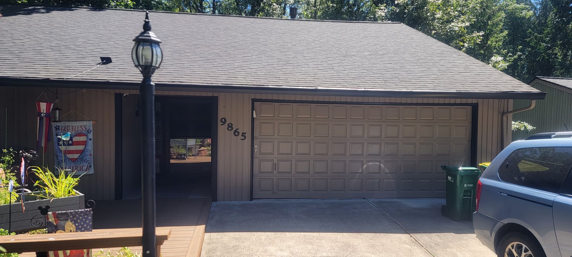 A tan house with a garage and a black lamp post. A blue minivan is parked in the driveway.