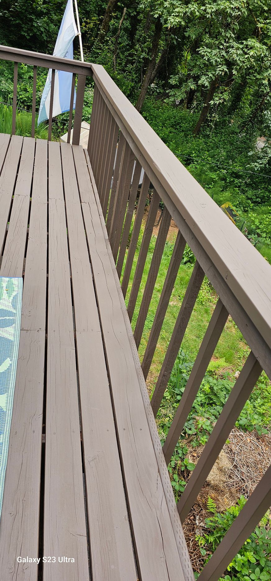 Wooden deck with brown railing, overlooking green foliage.
