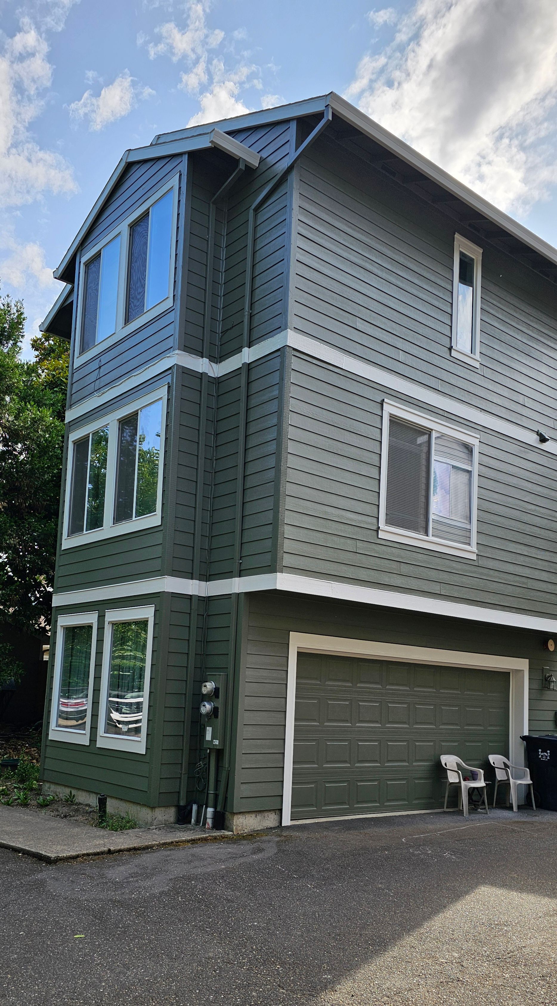 Three-story green building with a garage, windows, and white trim against a cloudy sky.