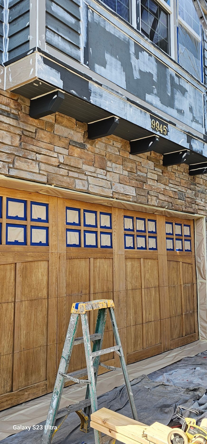 Exterior view of a building with stone facade, garage doors, and a ladder.