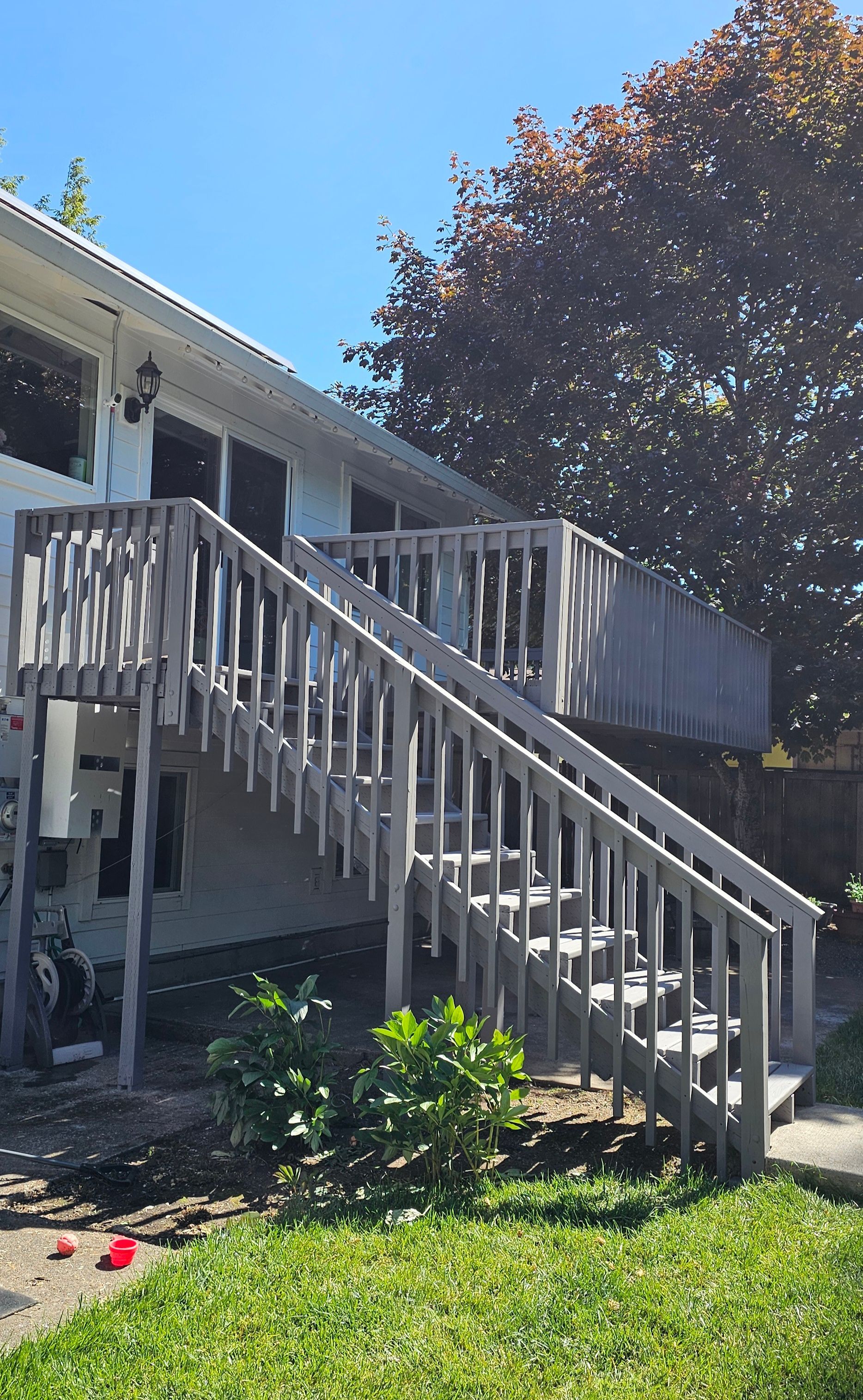 Wooden outdoor staircase and deck on a two-story building. The wood is weathered, and a tree is visible.