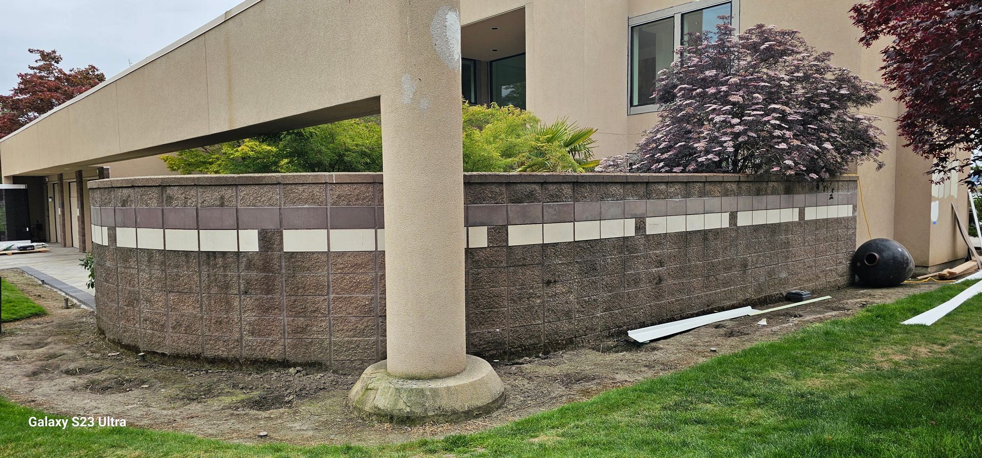 Curved concrete wall with horizontal white and brown sections, next to a building and lawn.