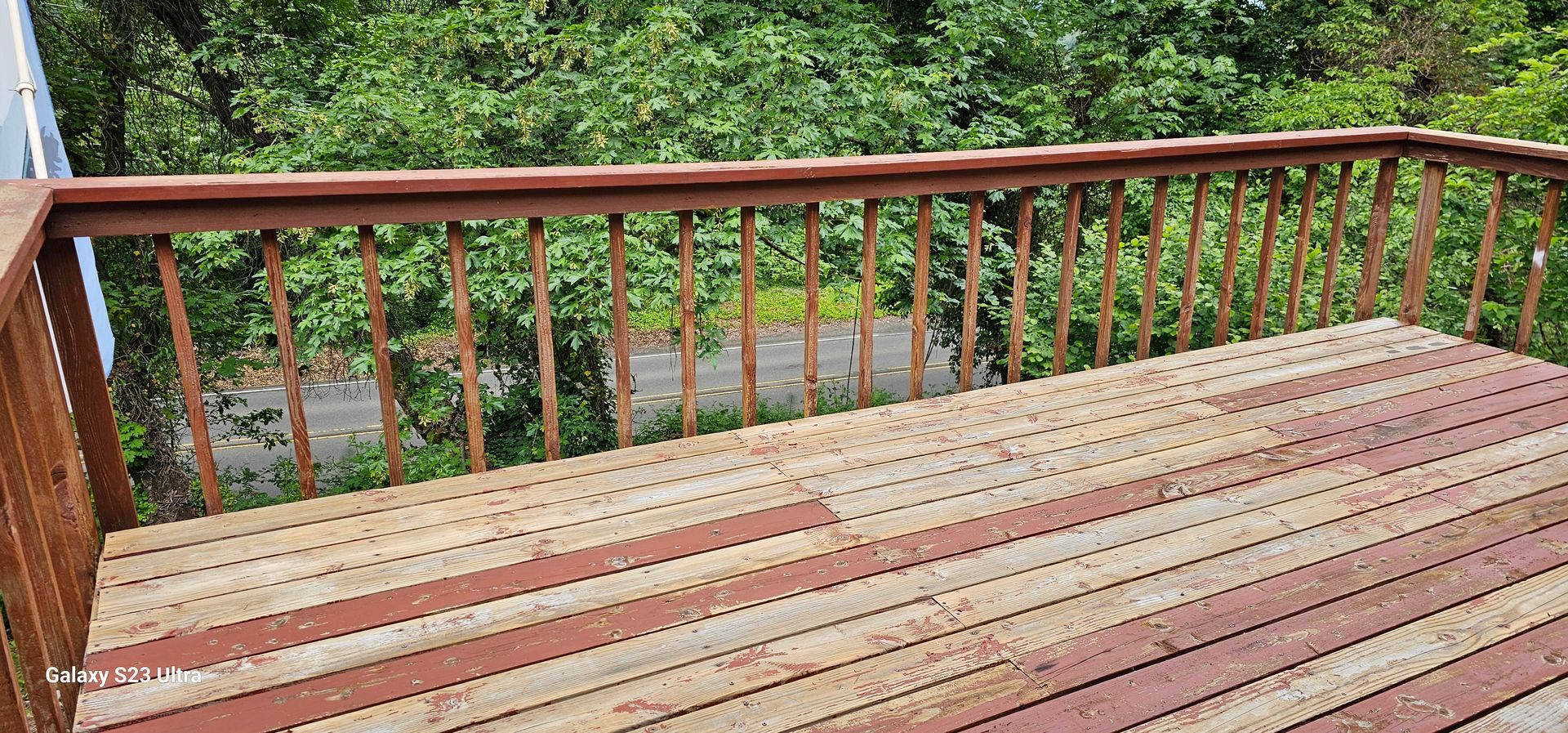 Wooden deck with railing overlooking a lush green backdrop of trees.