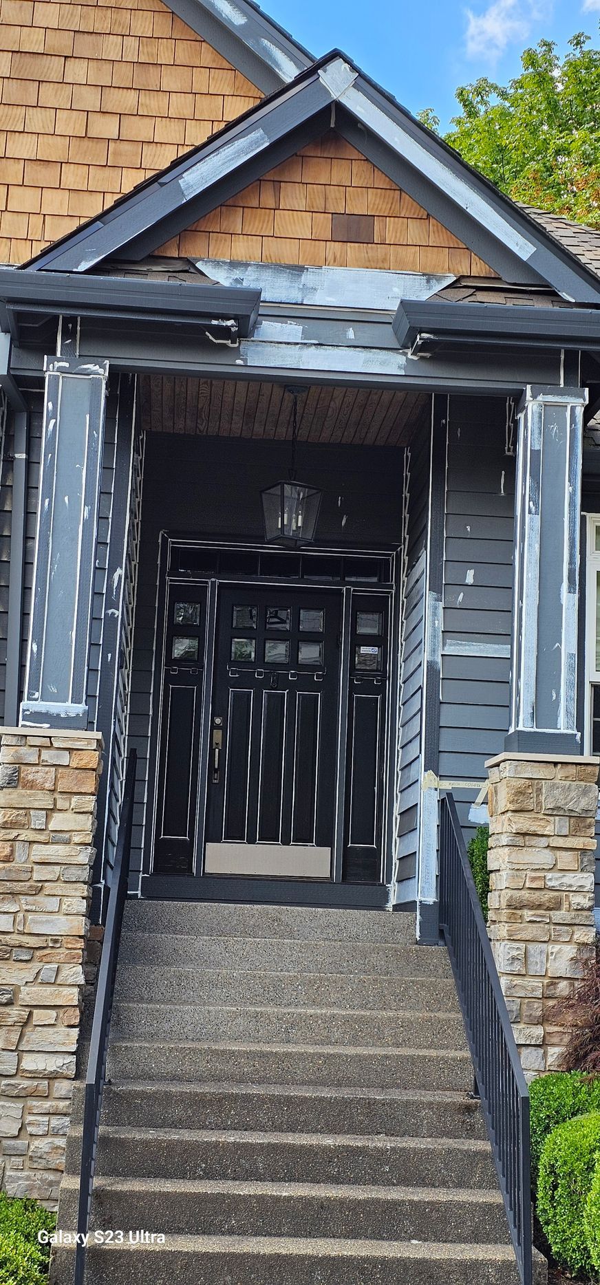Dark gray front door with stone steps, columns, and brown shingle roof.