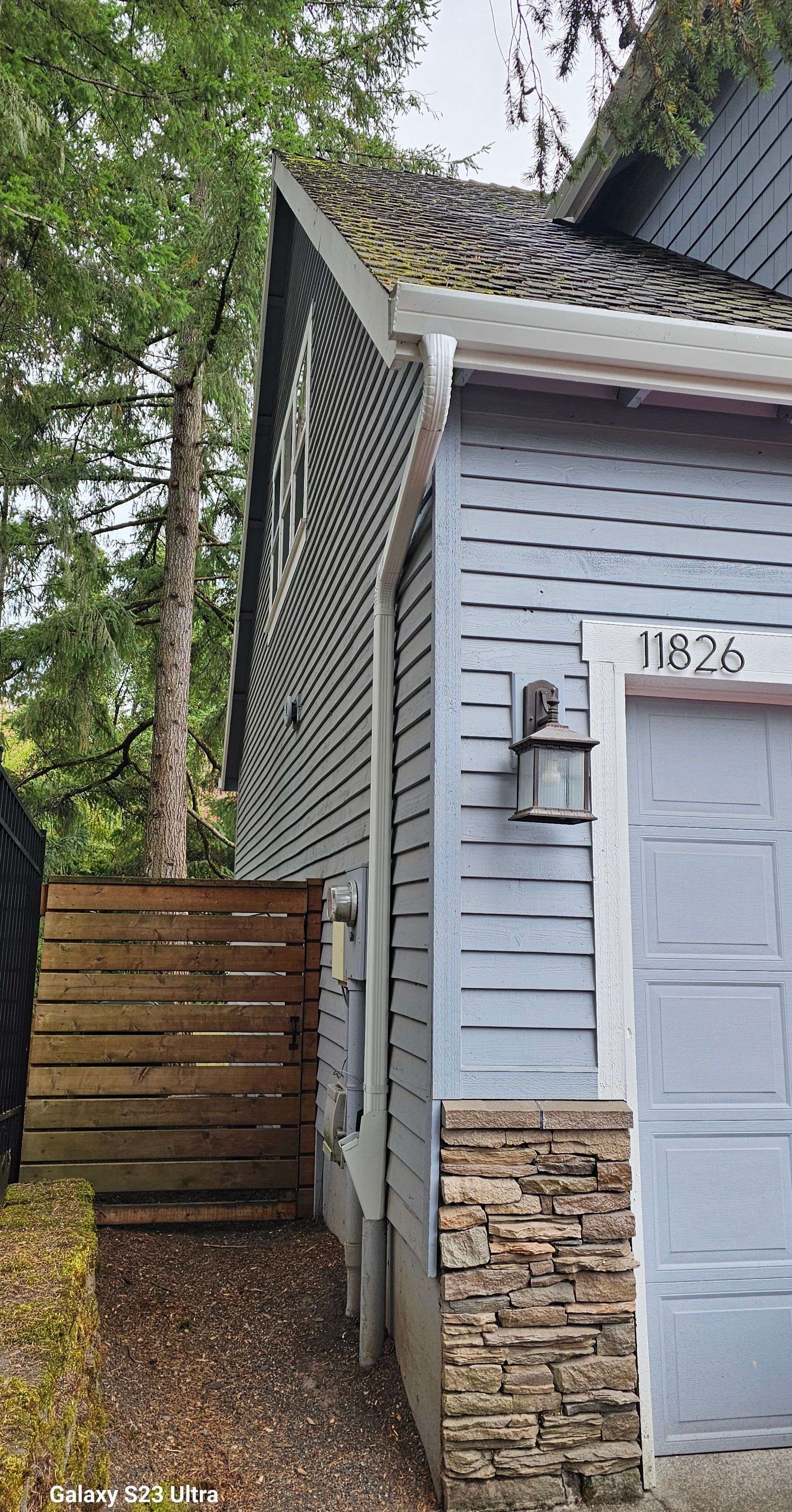 A blue house with a garage door and stone accents, wooden fence, trees, and address 1162b.