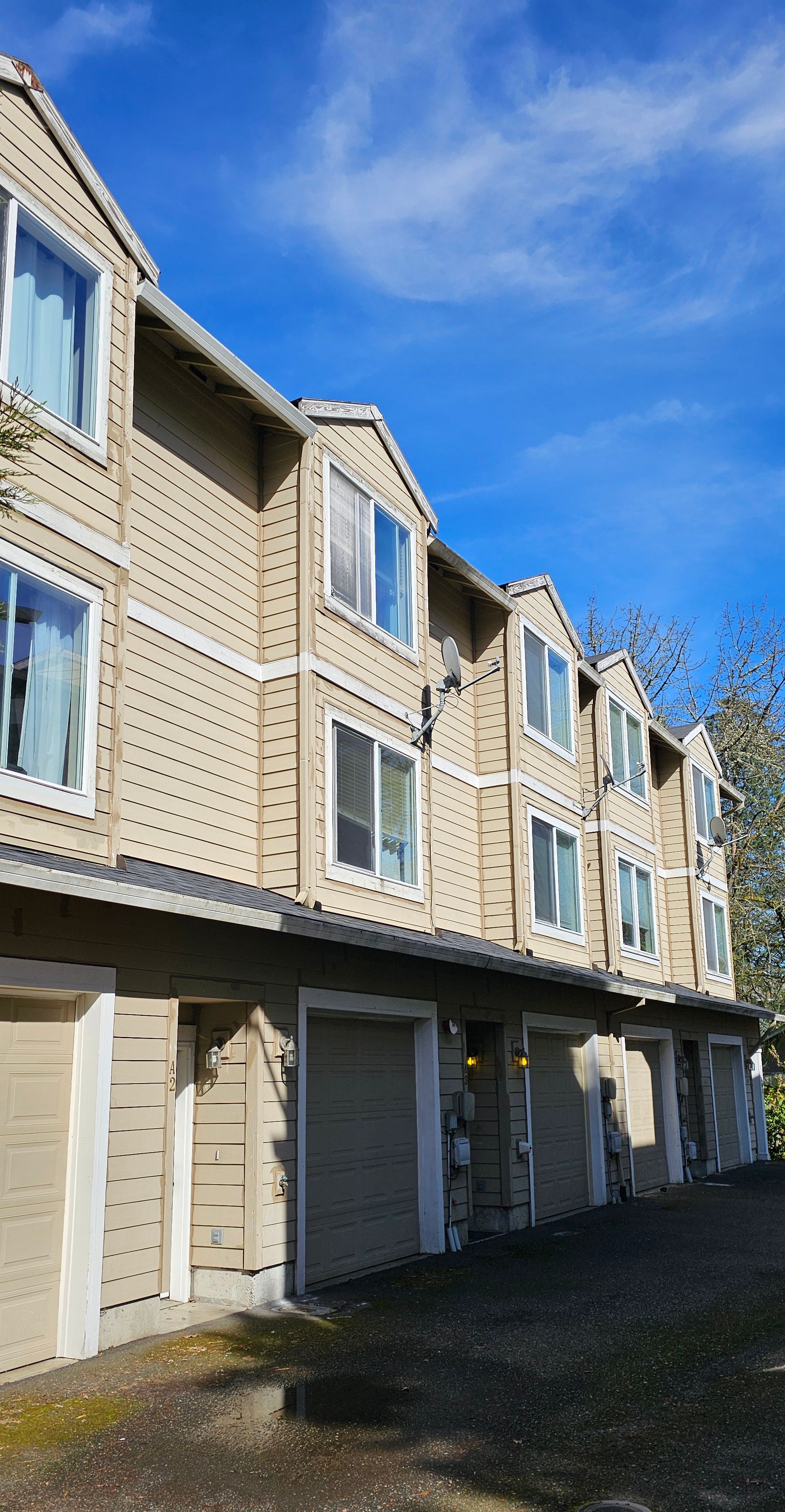 Tan townhouses with white-framed windows and garage doors against a blue sky.