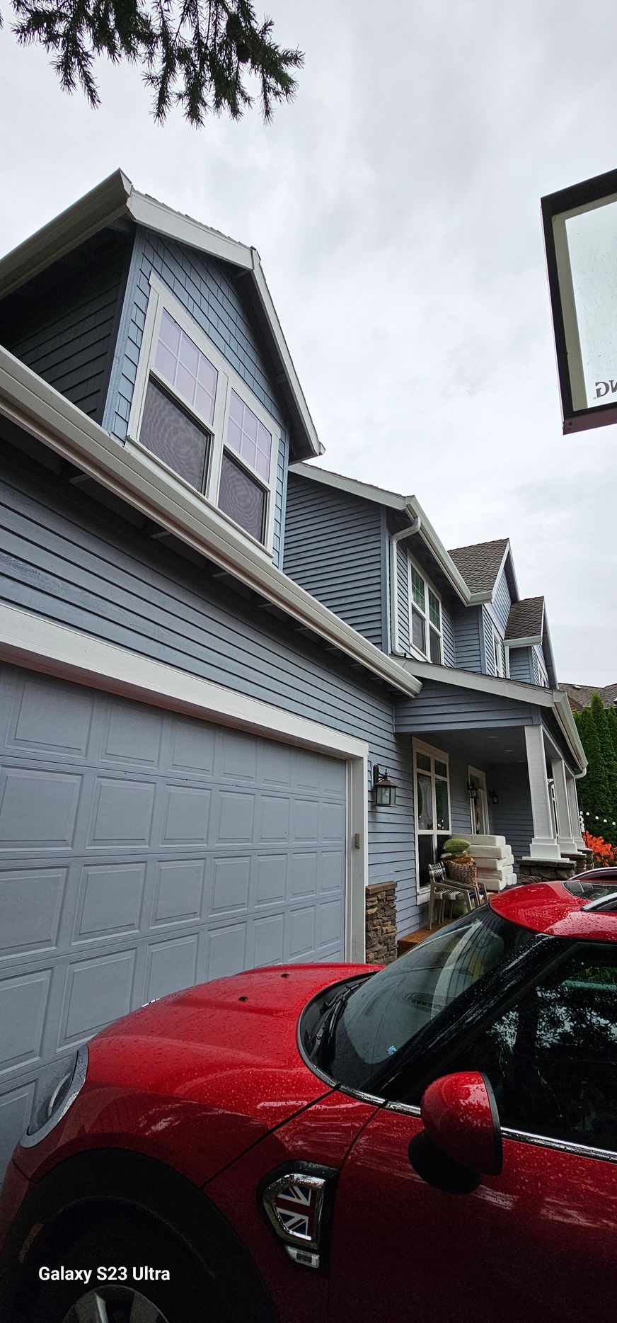 Red car parked in front of a blue house with gray garage door. Overcast sky.