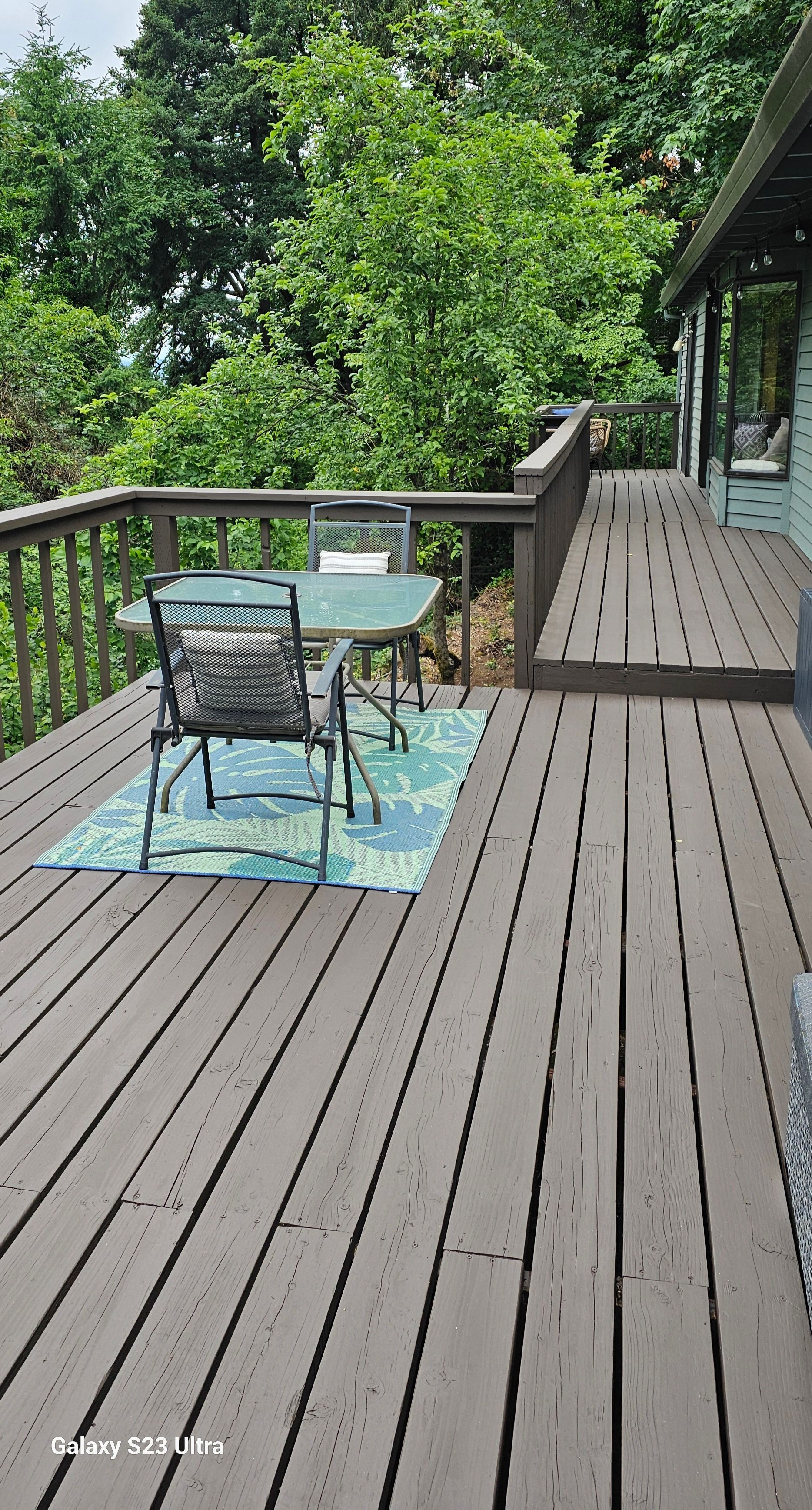 Wooden deck with table and chairs overlooking lush green trees.