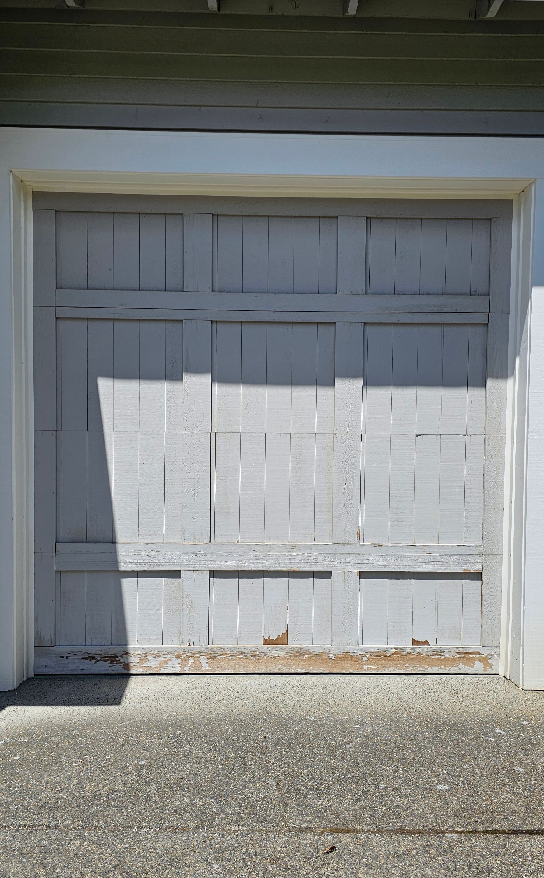 A weathered gray garage door with peeling paint.