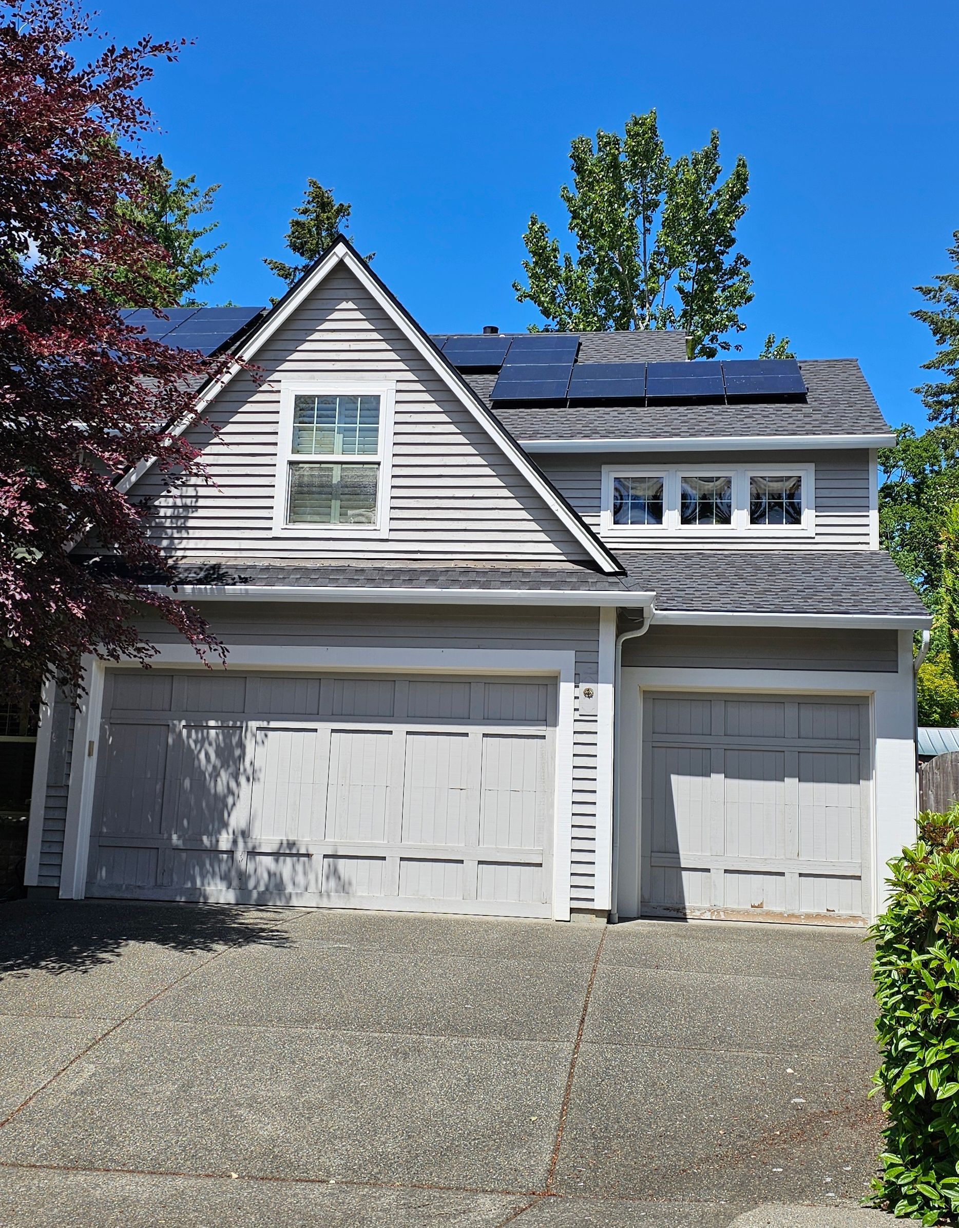 House with gray siding and garage doors, solar panels on the roof, and a clear blue sky.