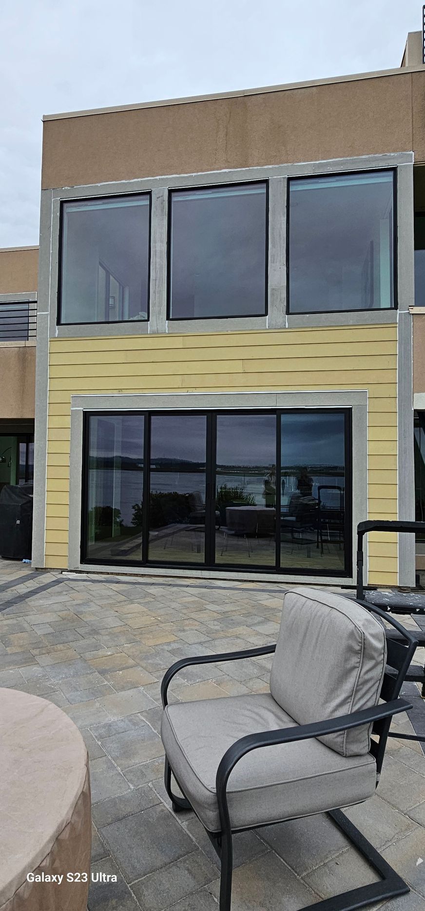 A modern building with large windows and a patio with a chair overlooking a body of water.