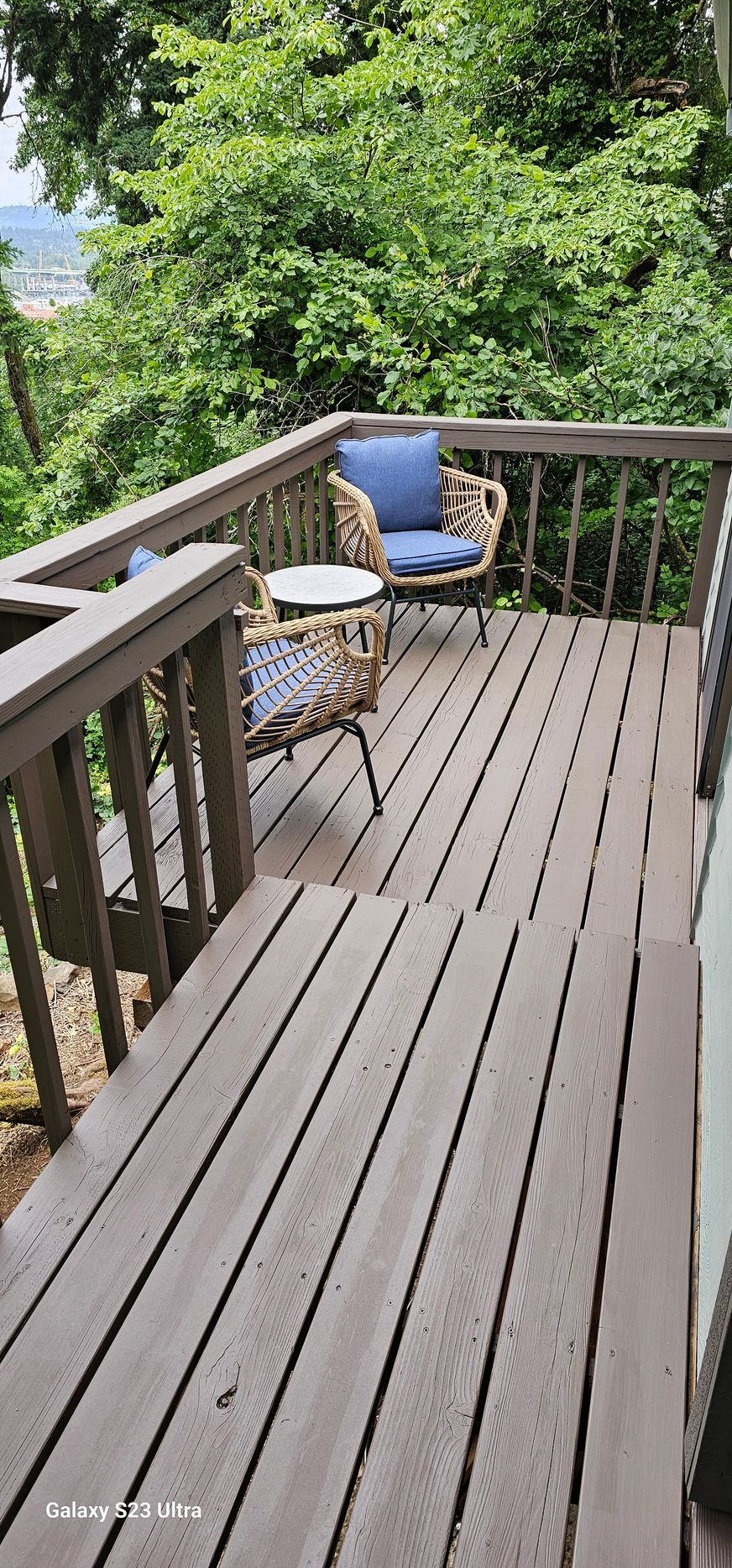 Wooden deck with wicker chairs and table overlooking lush green trees.