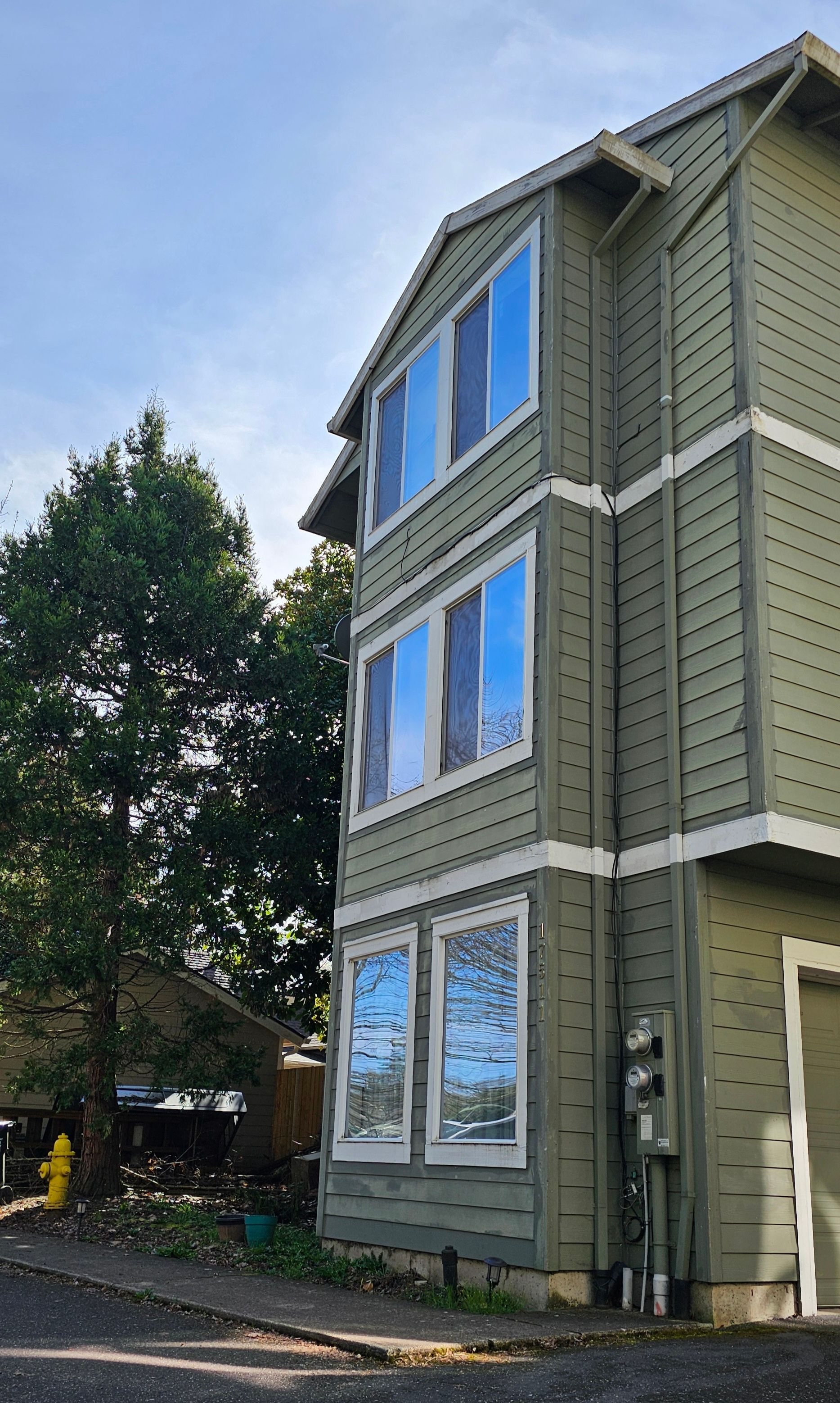 Three-story green building with multiple windows. A tree is on the left, and a garage on the right.