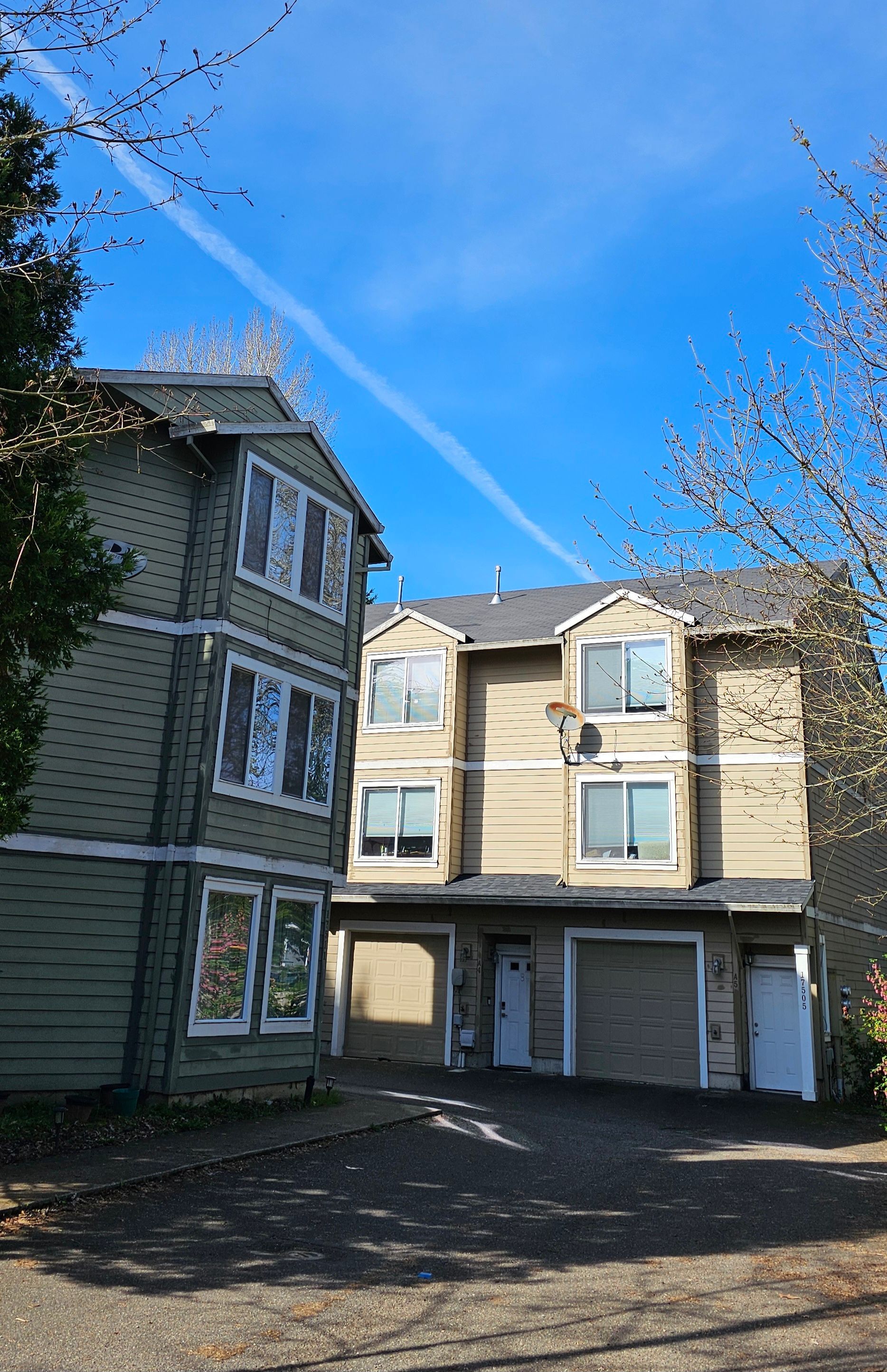 Apartment buildings, one green and one tan, with garages under a blue sky, branches in view.