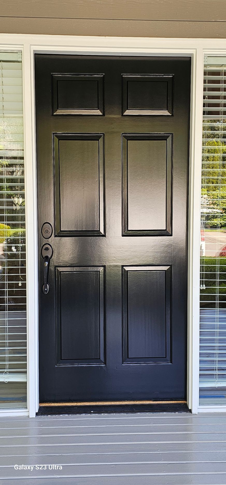 Black front door with six panels, white trim, and windows on either side.