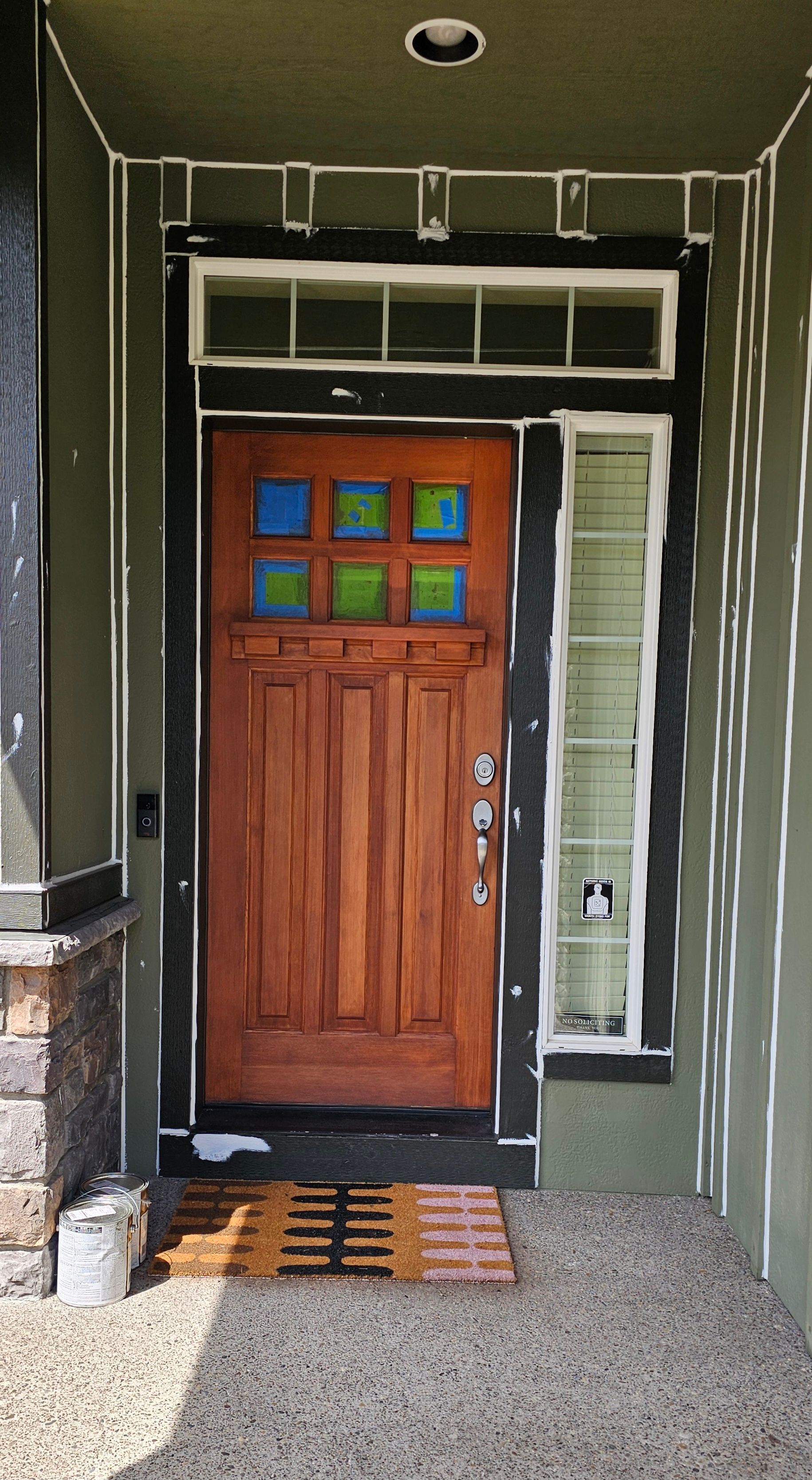 Wooden front door with blue and green stained glass, flanked by a narrow window.