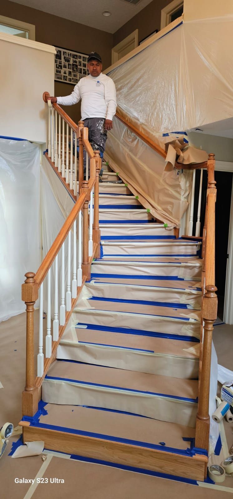 Person standing on a staircase, preparing for painting. The steps are covered with protective tape and paper.