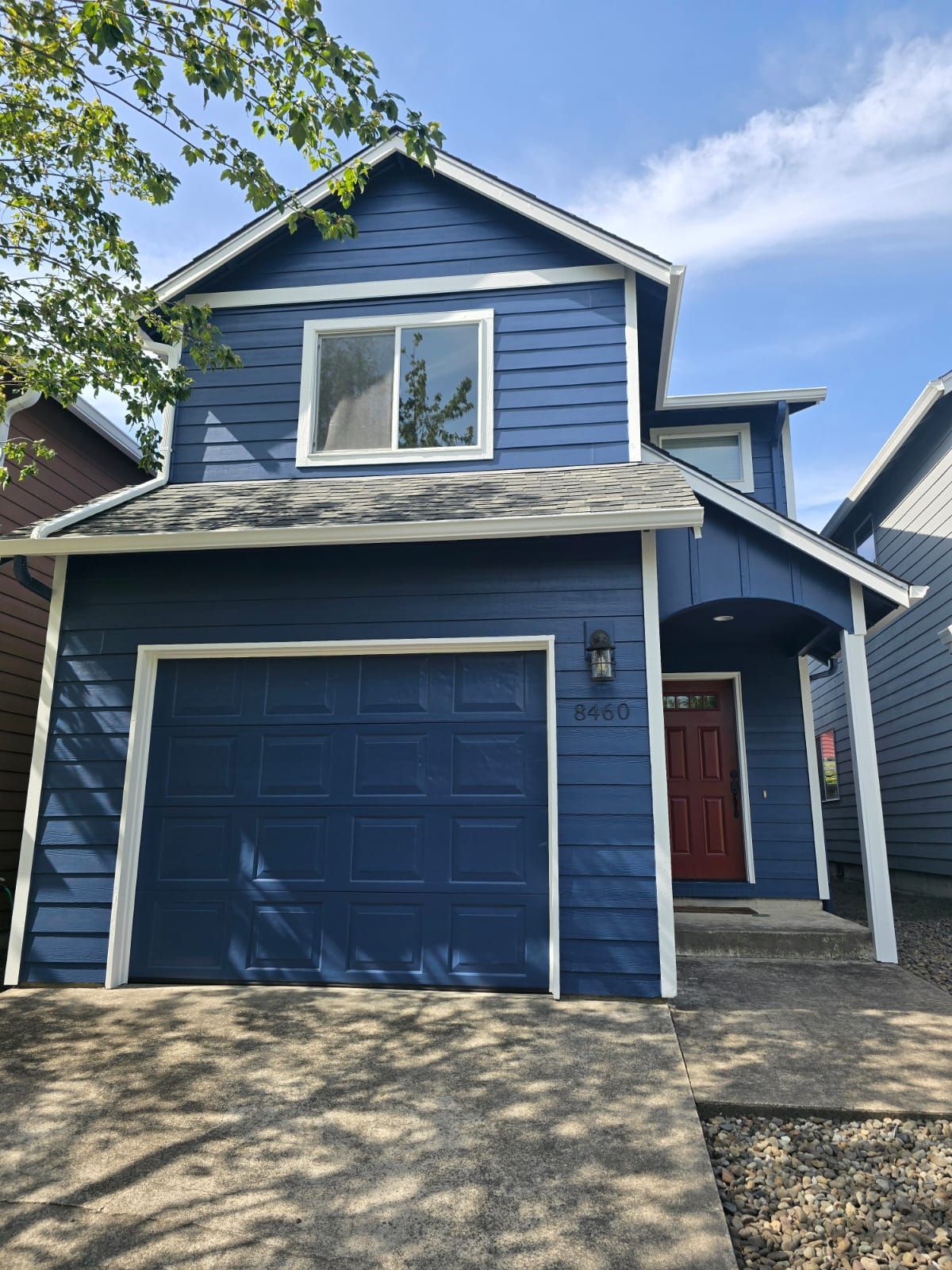 Two-story blue house with a red front door, a garage door, and a clear sky above.