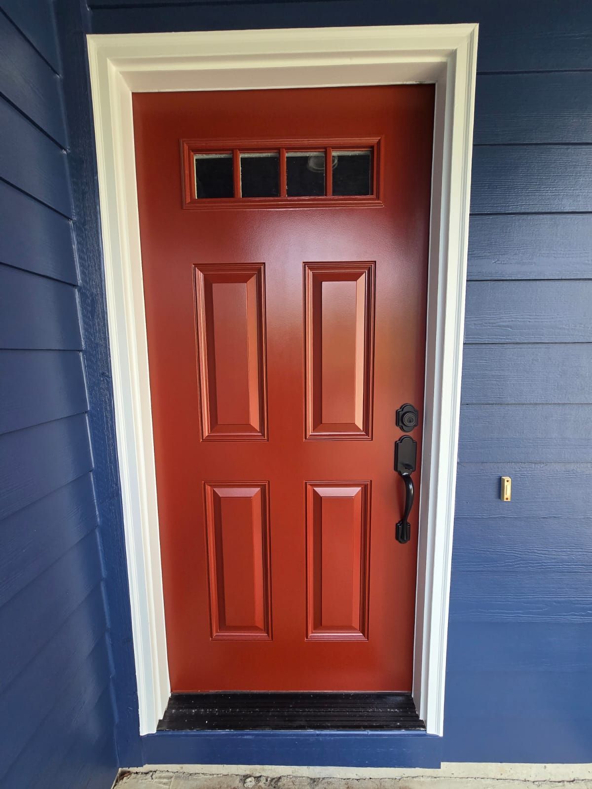 Red front door with glass transom, black hardware, white trim, on blue siding.