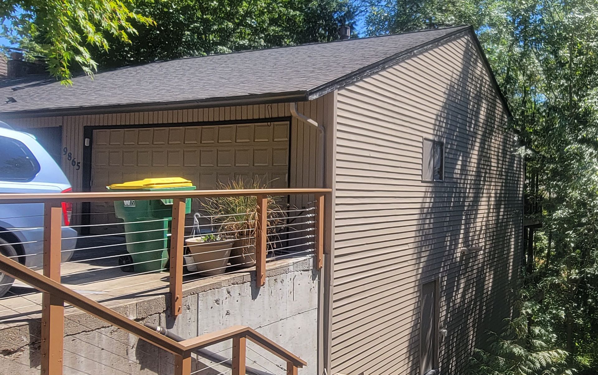 Tan-sided building with brown roof and garage door, next to a deck with brown railing.