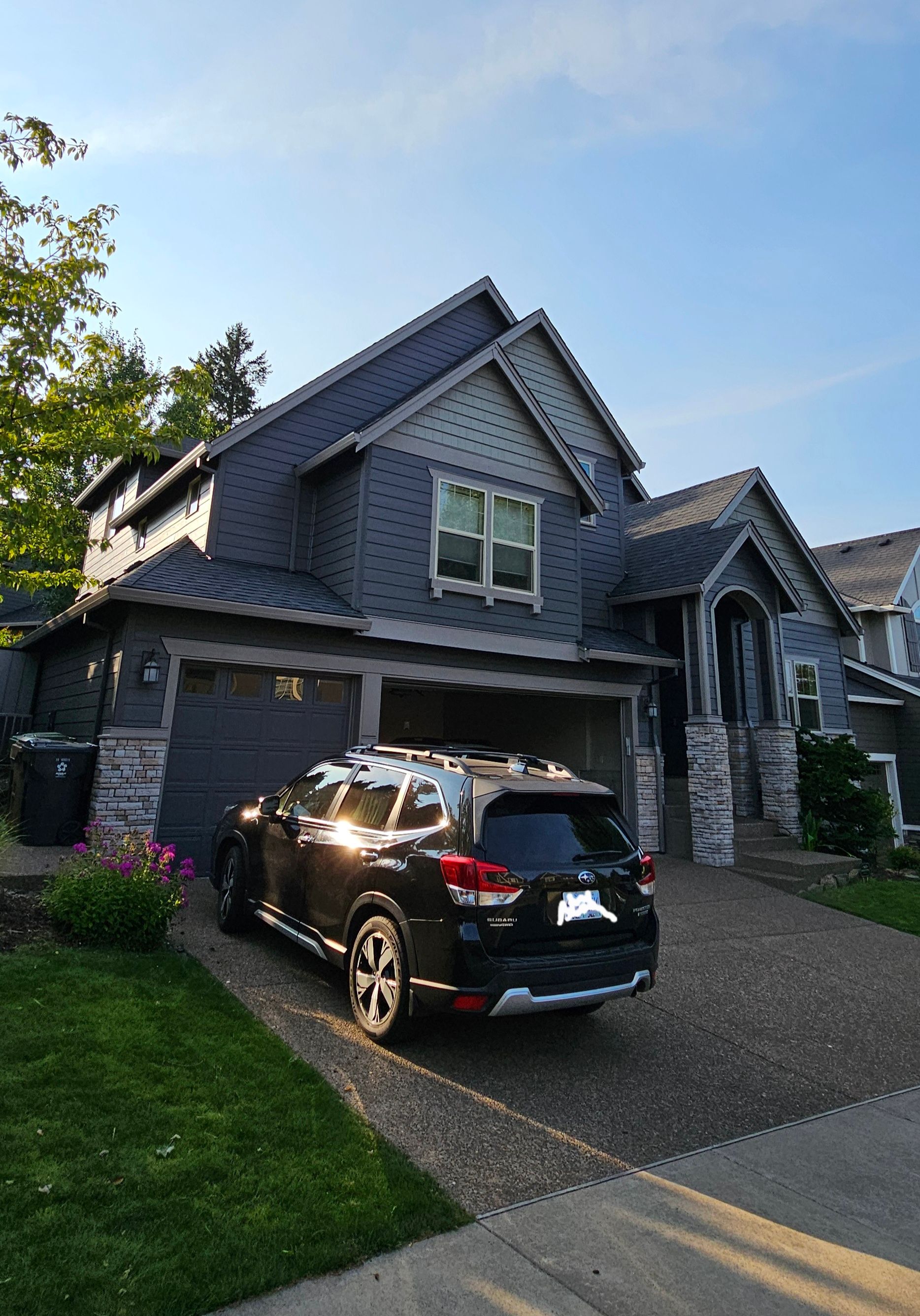 Black SUV parked in front of a gray two-story house with a blue roof on a sunny day.
