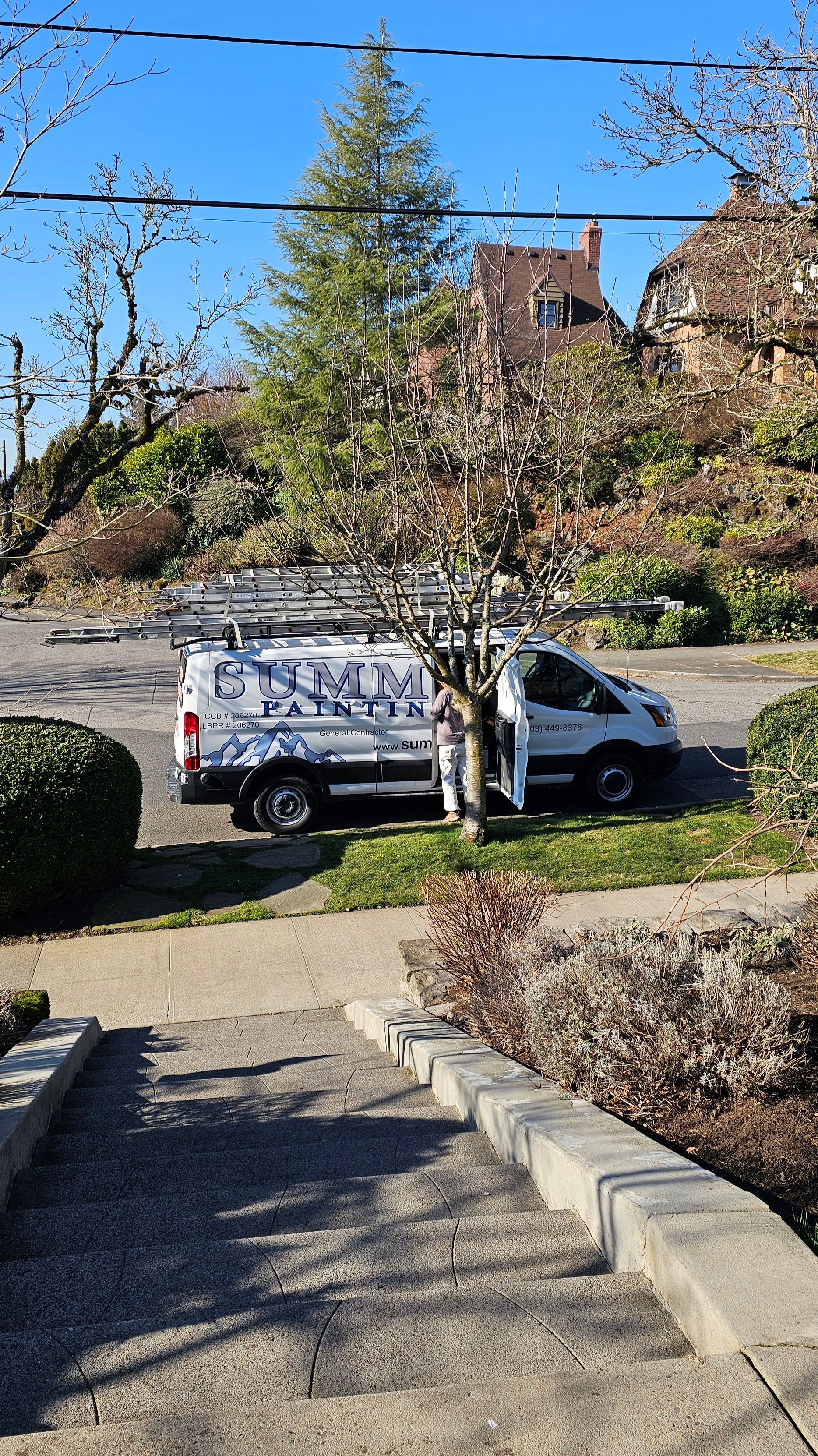 White service van parked on a street; door open. Trees and a house in the background on a sunny day.