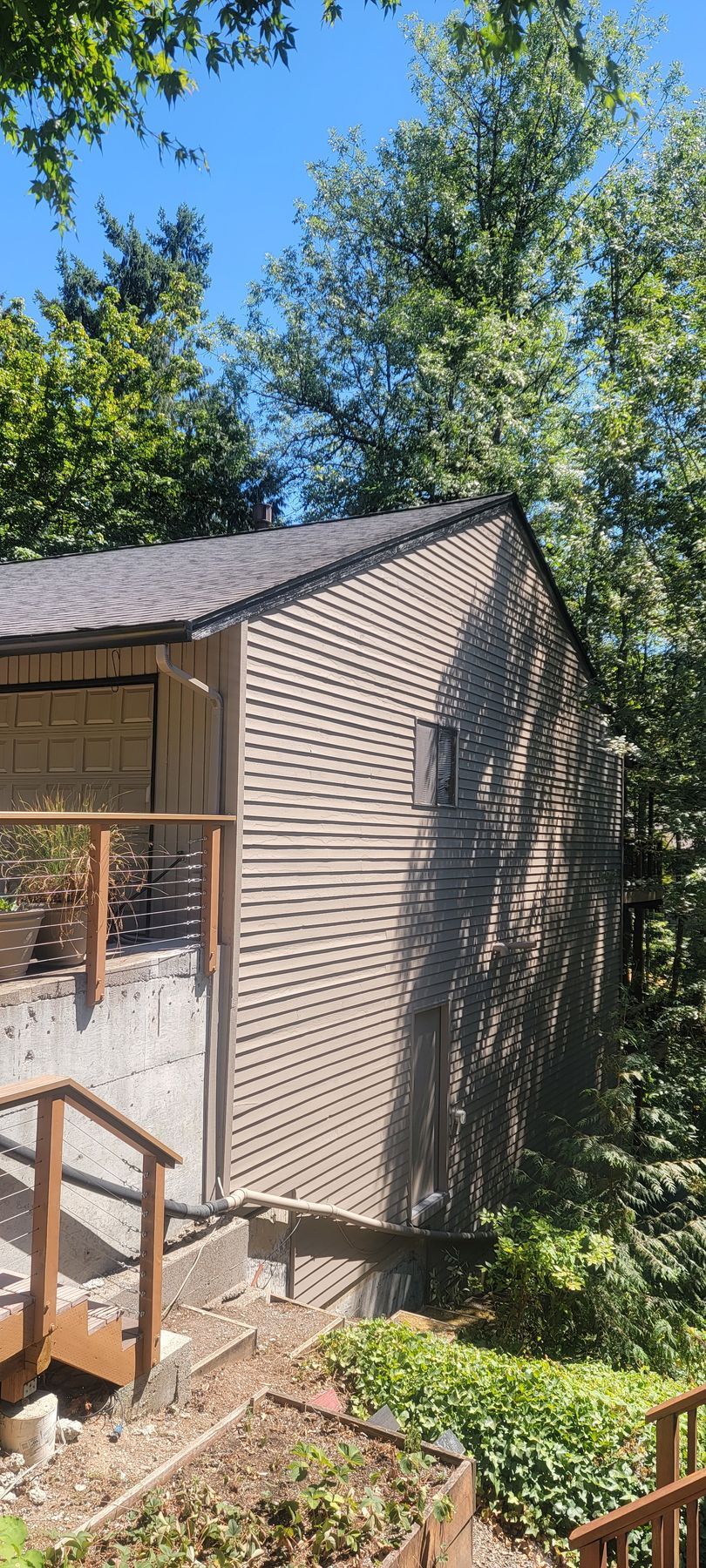 A two-story building with wood siding and a wooden deck, surrounded by trees under a clear blue sky.