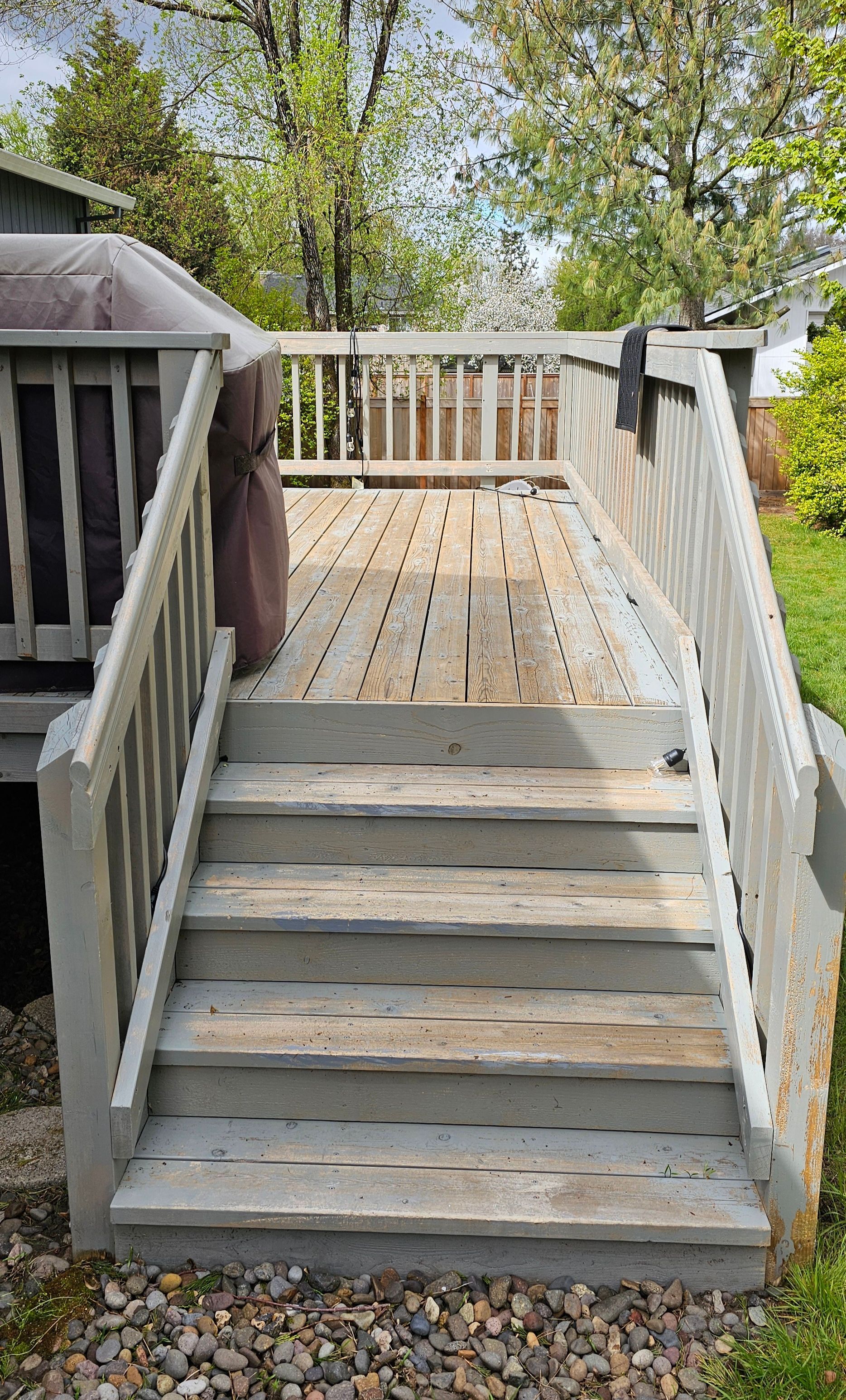 Wooden deck with stairs, gray weathered planks, handrails, pebble ground.