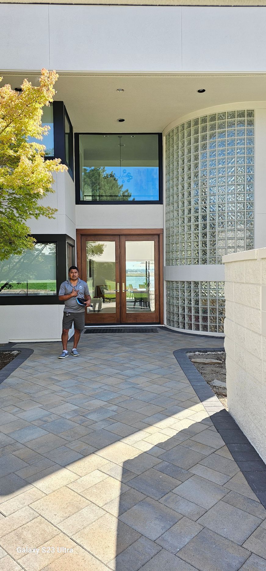 A person stands on a paved path in front of a modern house with a glass block wall.