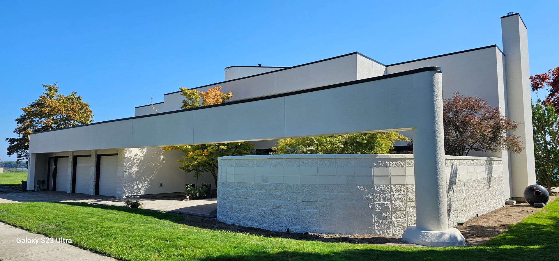 Modern white building with flat roof and textured stone wall, green grass, and blue sky.