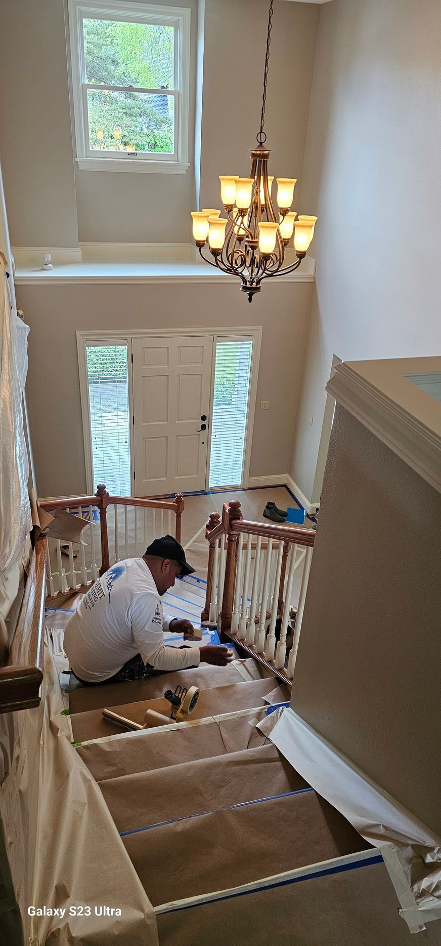 Person working on stairs in a home, painting. Chandelier hangs above.
