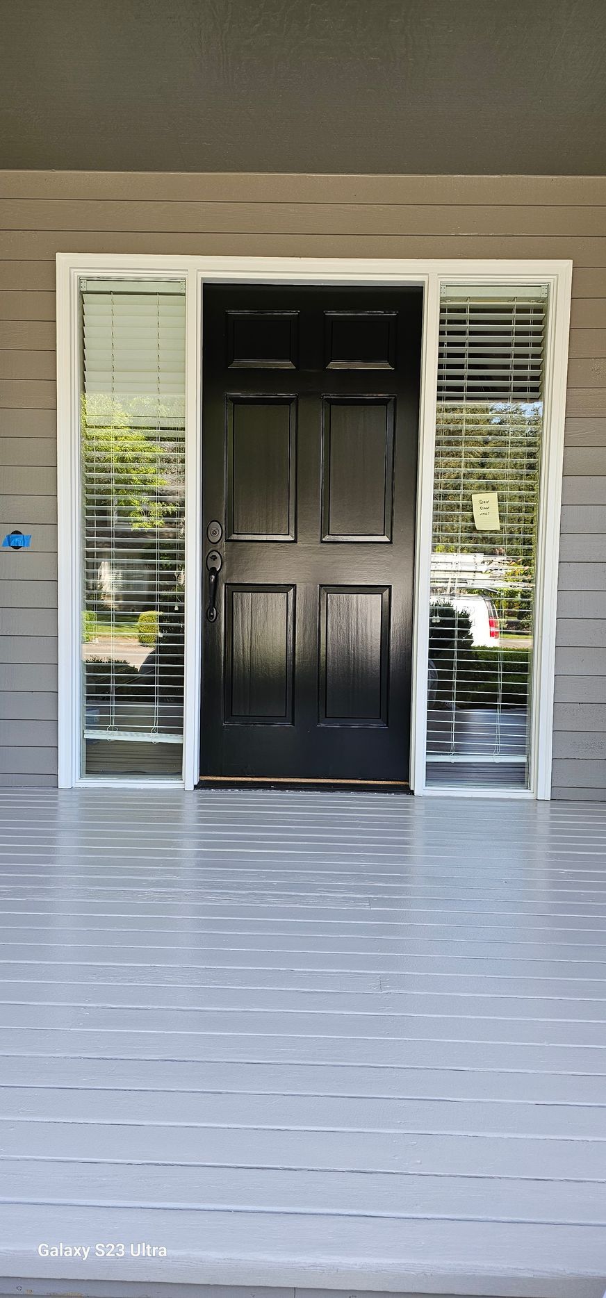 A black front door with white trim, flanked by windows with blinds, leads to a gray porch.