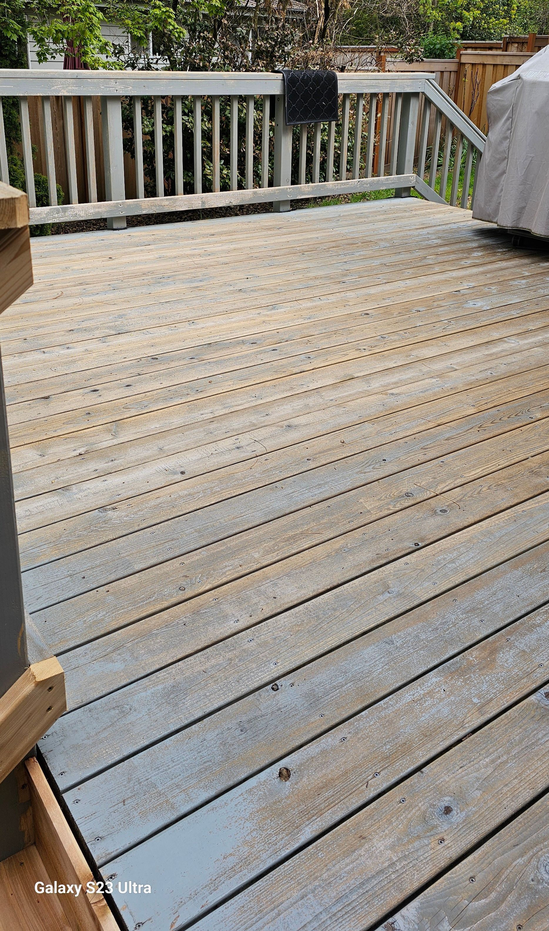 Wooden deck with weathered planks, railing, and a covered item on the right.