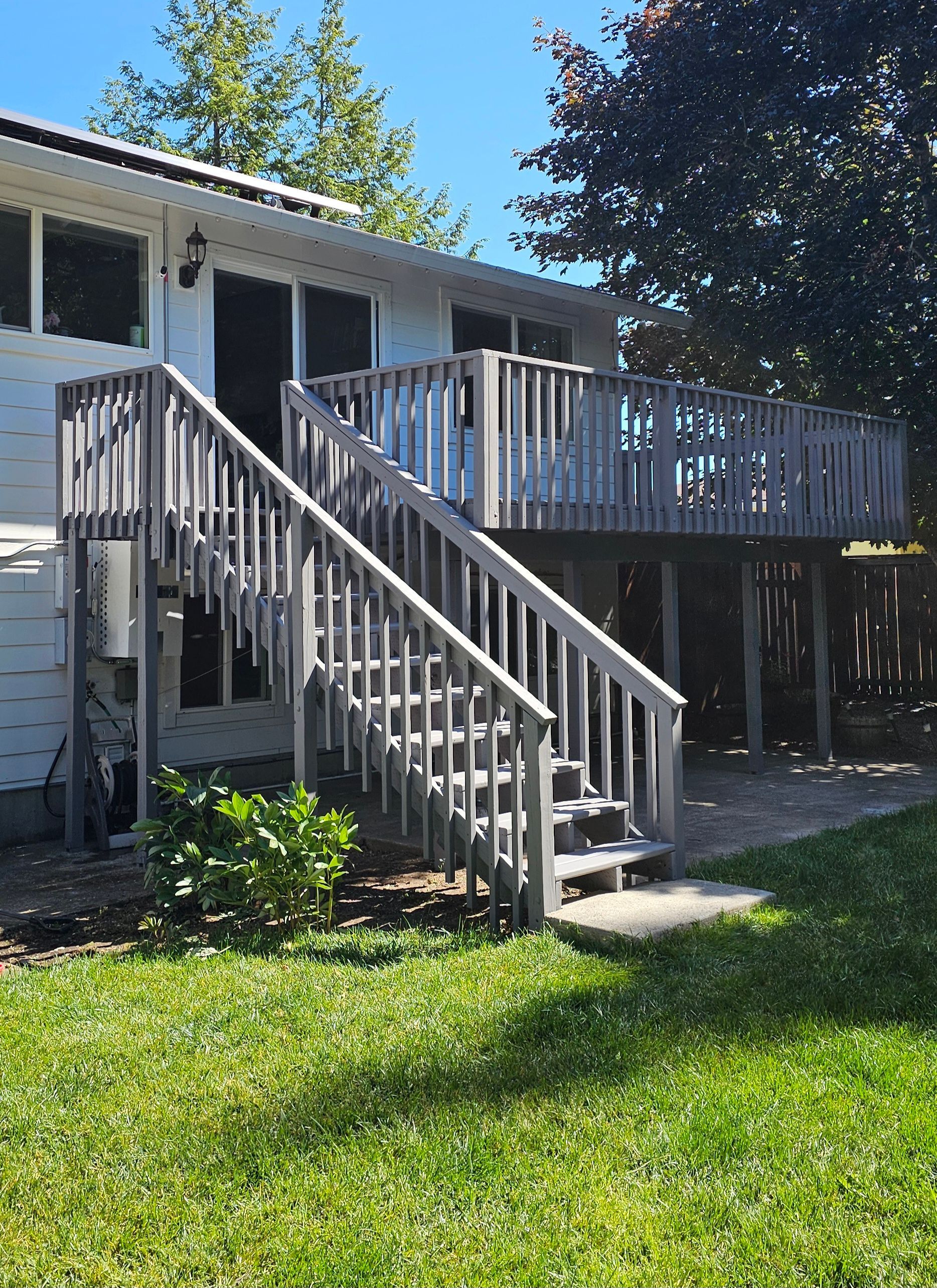 Wooden deck and stairs on the back of a white house, set in a grassy yard under a blue sky.