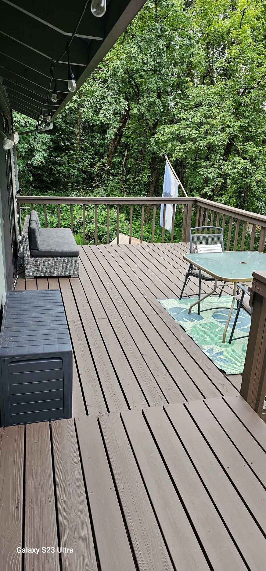 Wooden deck with a bench and table, surrounded by trees.