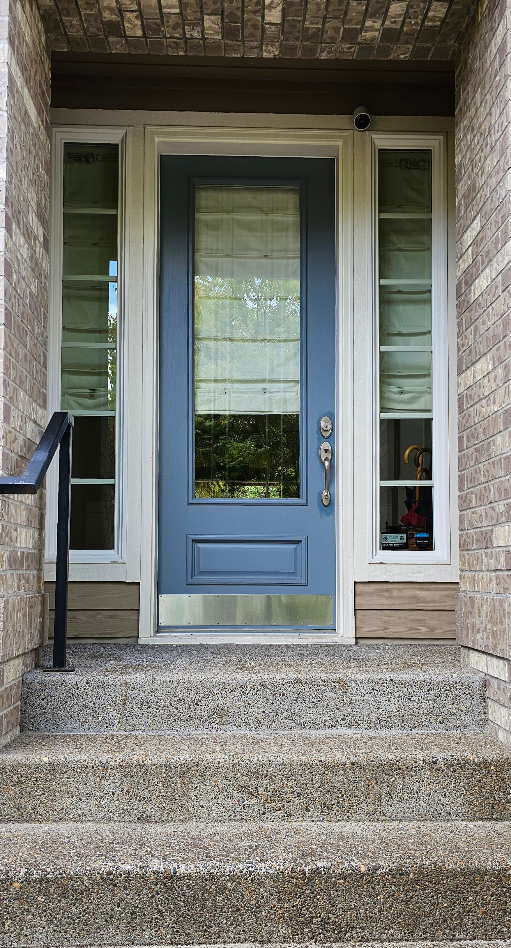 Blue front door with sidelights, steps, and brick facade.