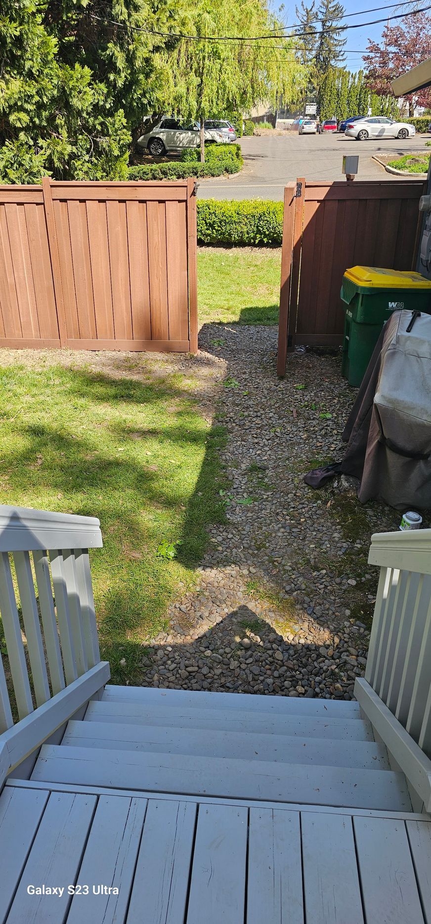 Wooden steps lead down to a grassy yard and gravel path, bordered by brown fences.