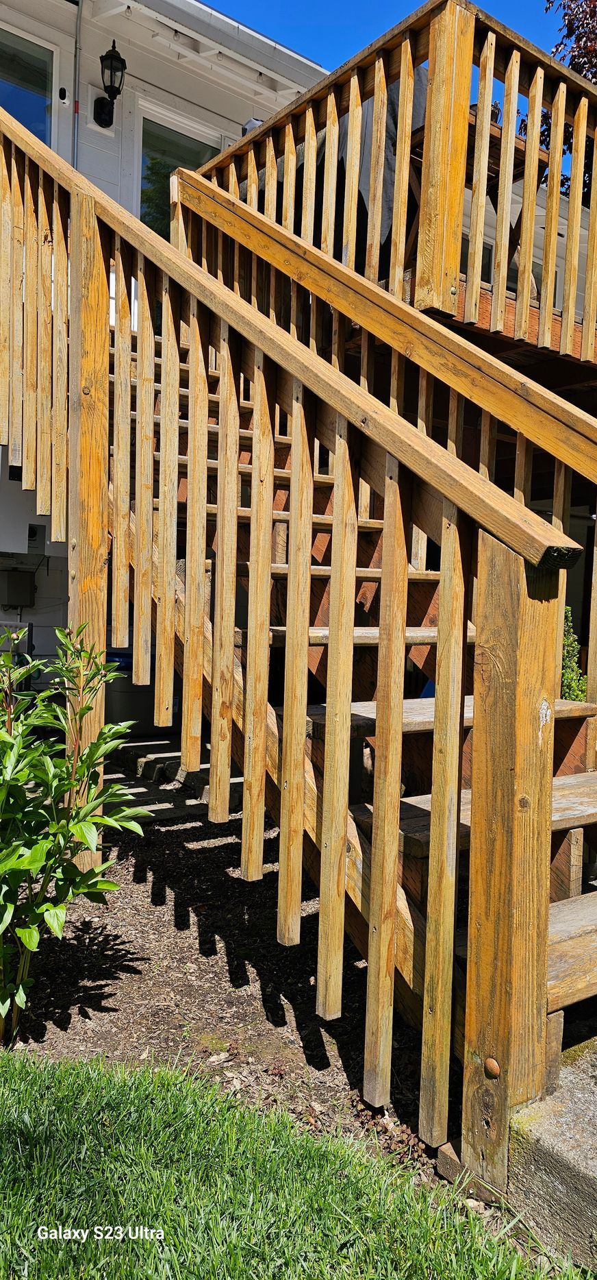 Wooden deck stairs with railings, outdoors. Brown wood, green grass, and blue sky.
