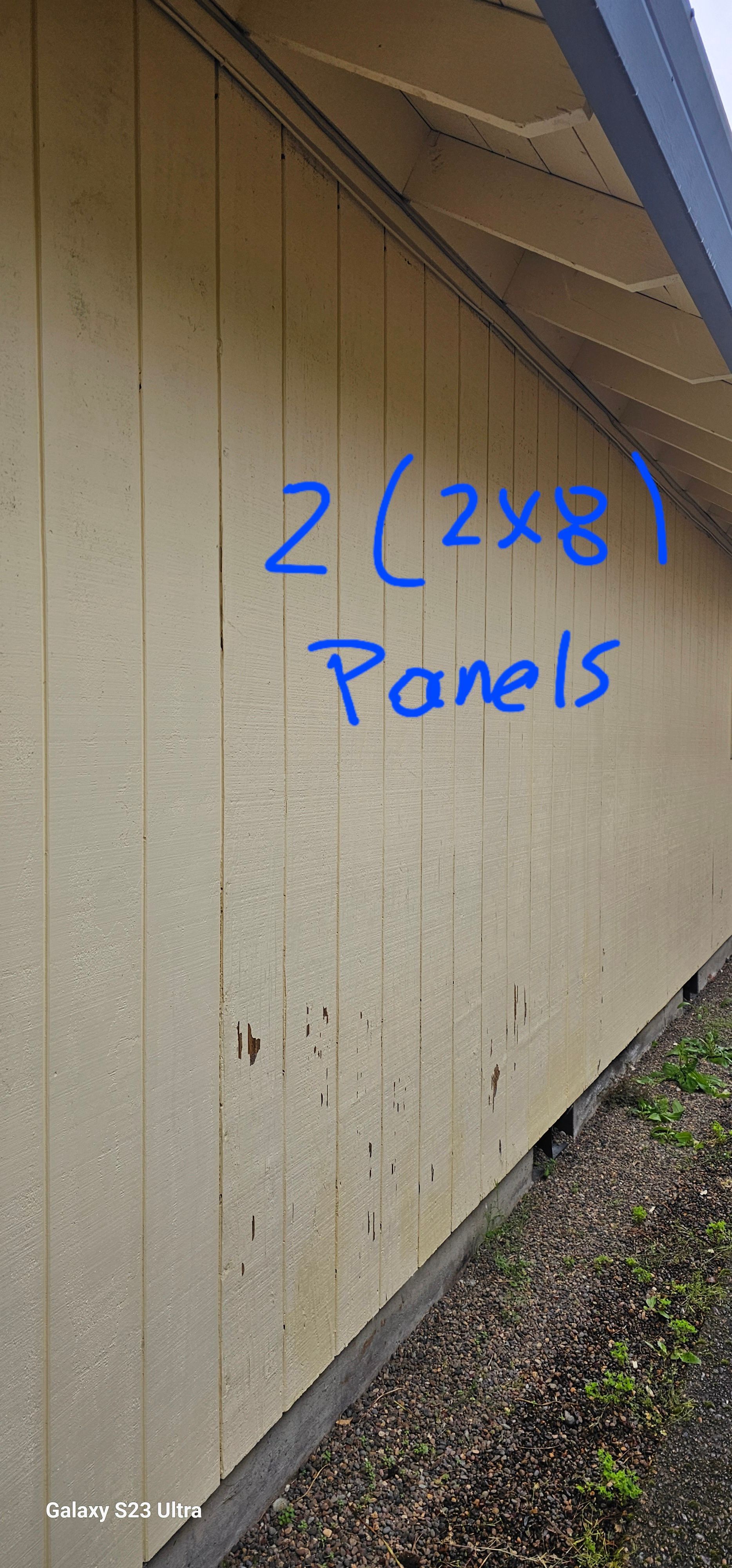 A light-yellow building's side has a handwritten note in blue, stating 