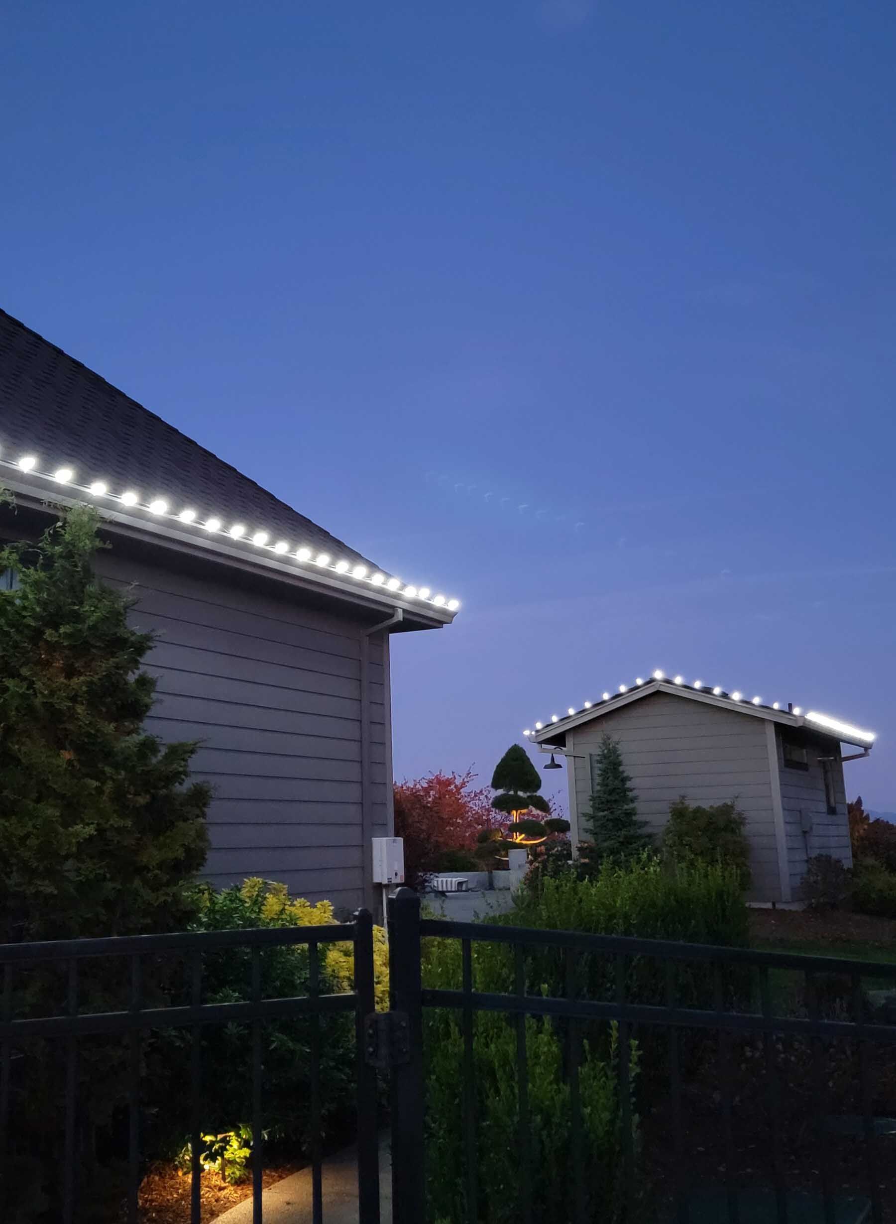 Two buildings with white string lights on their roof edges, under a dusky blue sky.