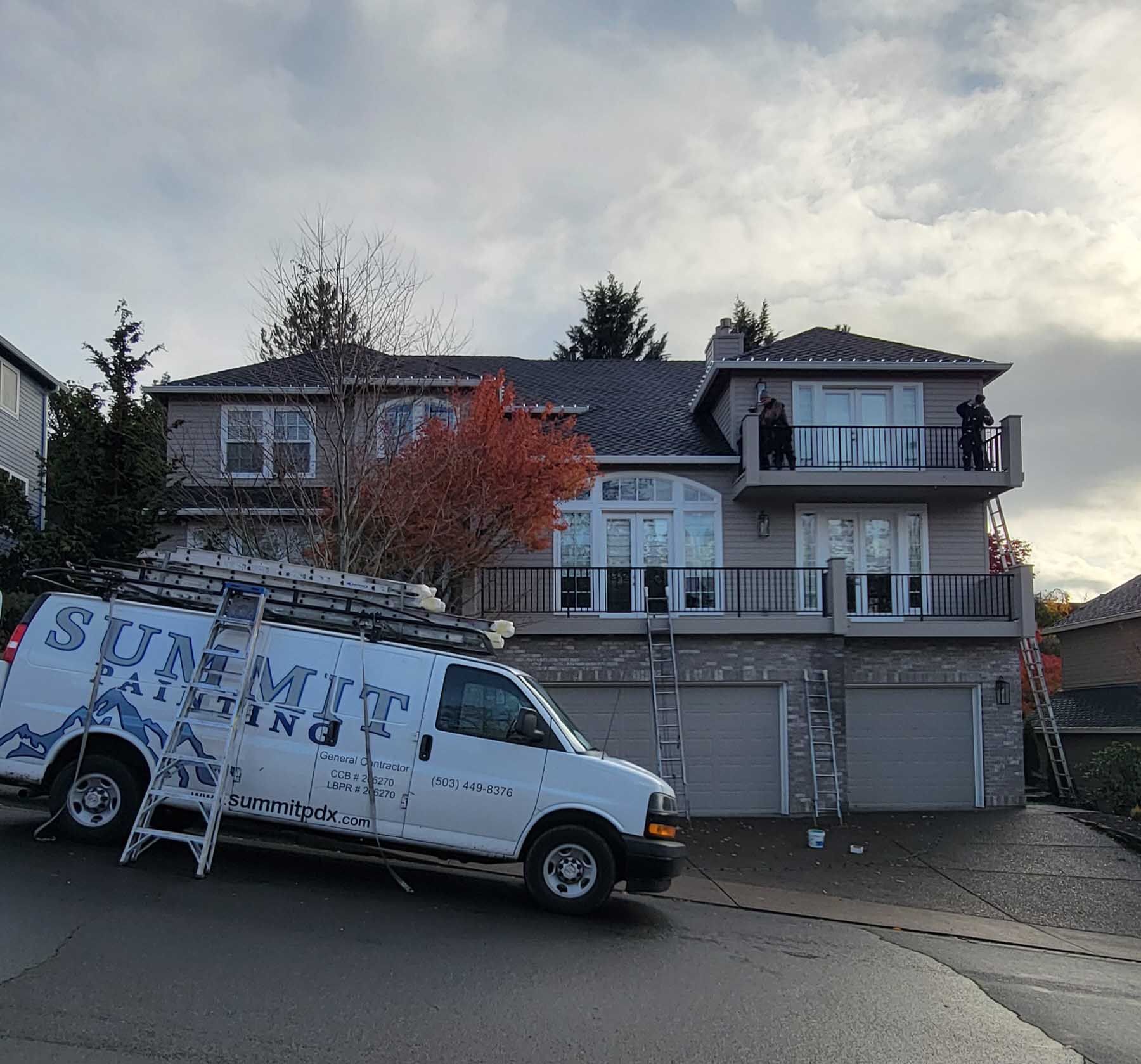 White van parked in front of a house. Workers on the roof with ladders. Cloudy sky.