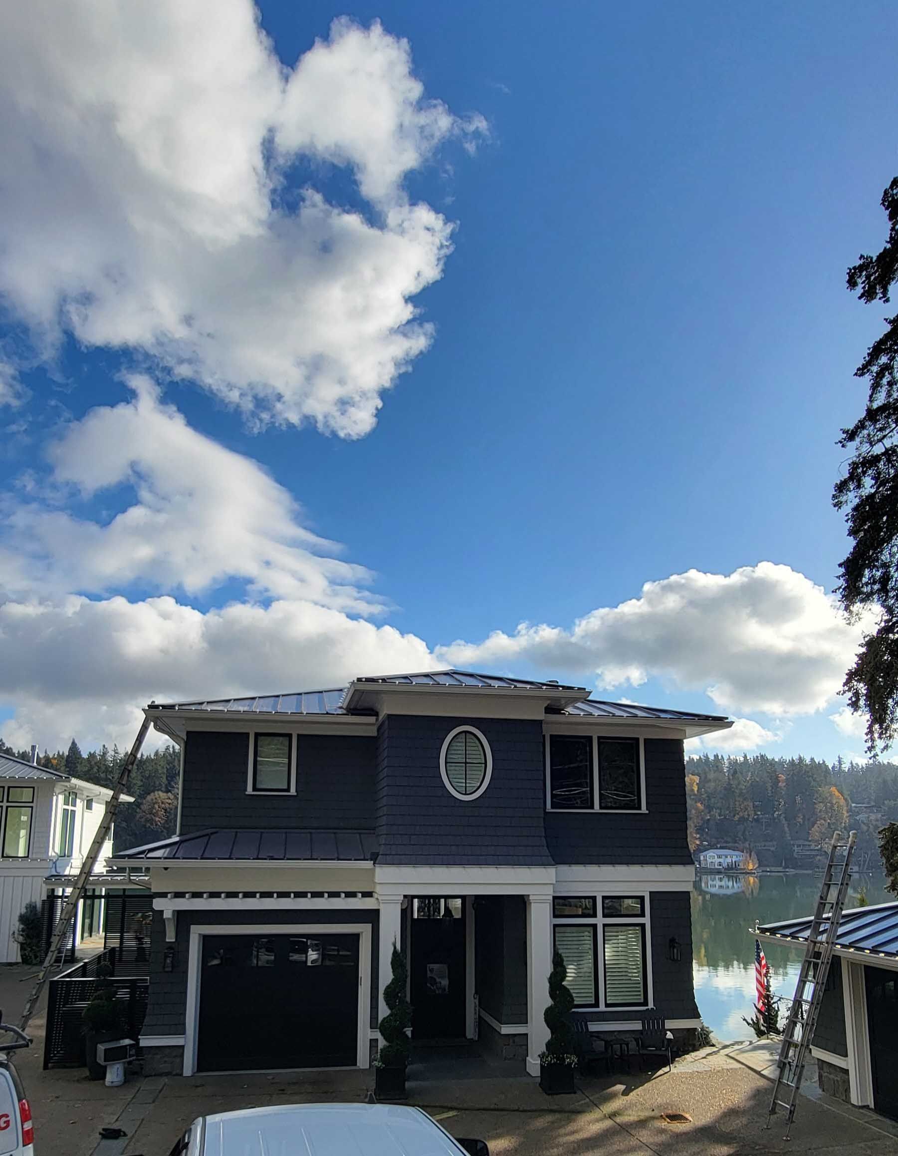 Blue two-story house with a black garage door under a partly cloudy sky next to a lake.