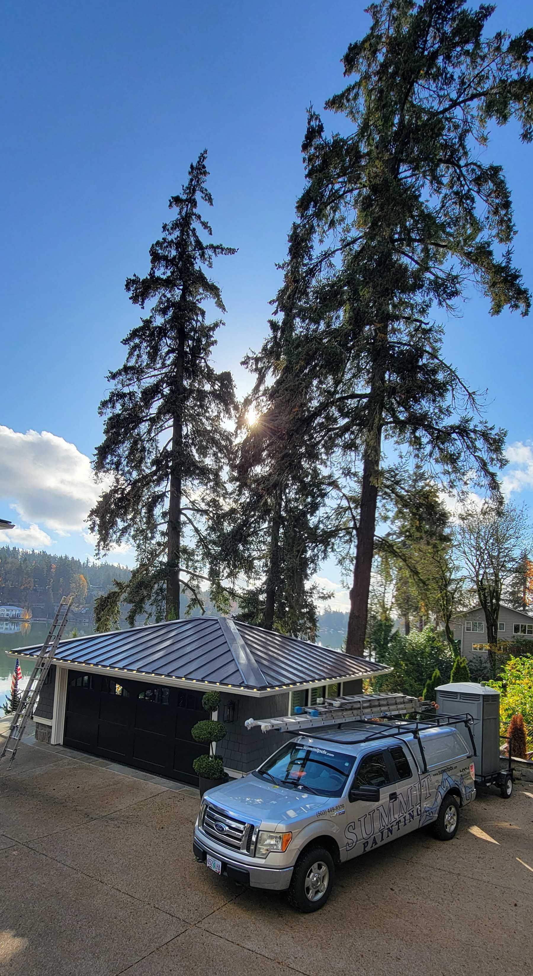 Silver pickup truck parked in front of a building with tall trees and sunny sky.