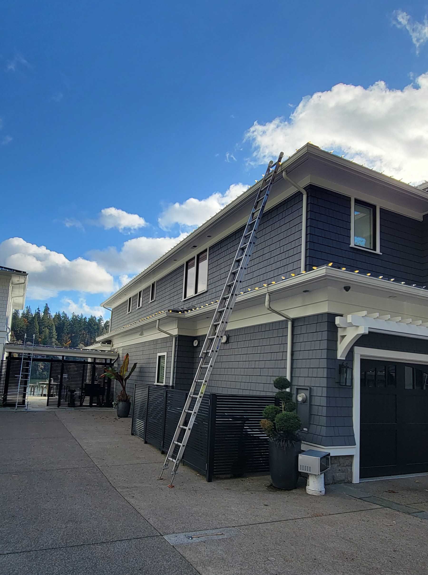 Ladder leaning against a two-story gray house with white trim against a blue sky.