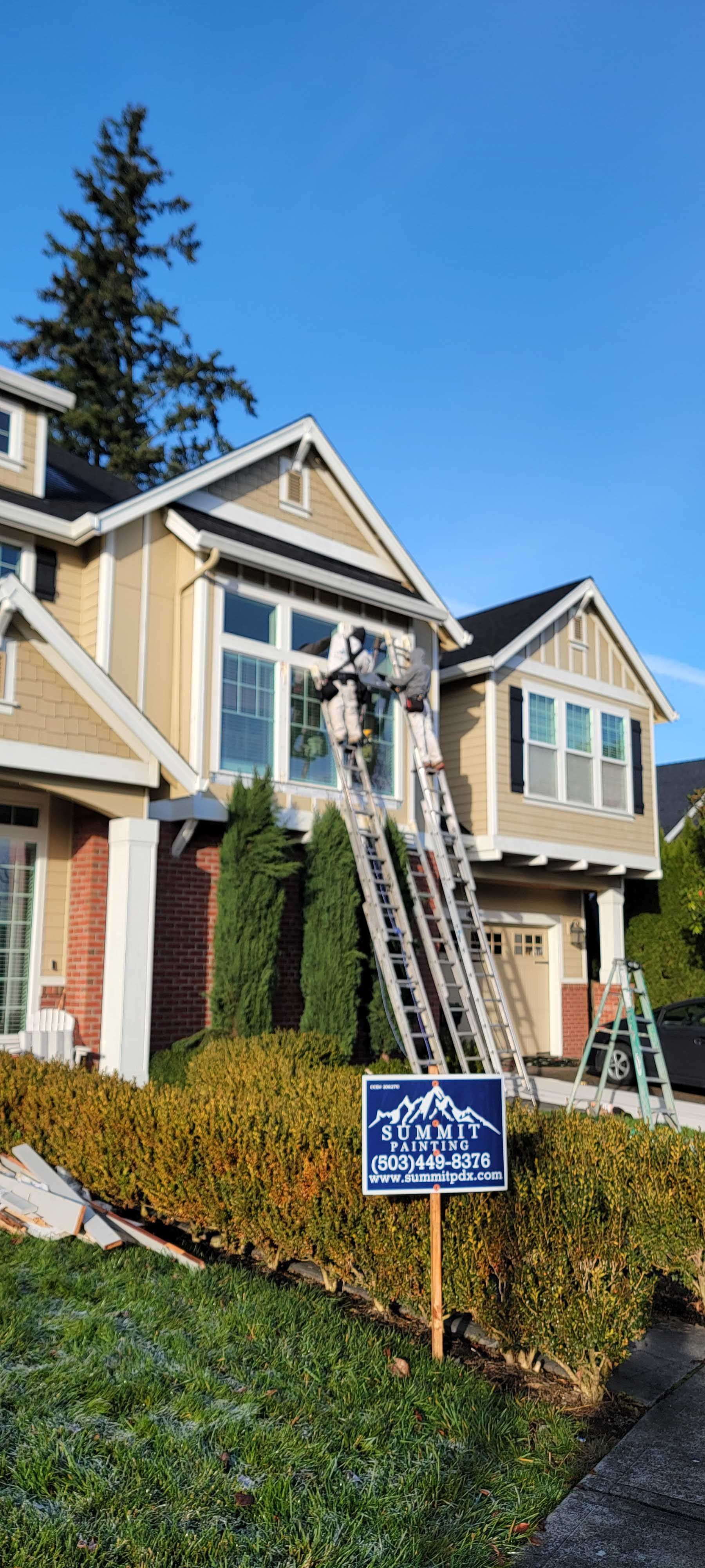 Person on a ladder painting the exterior of a two-story house with a sign in front.