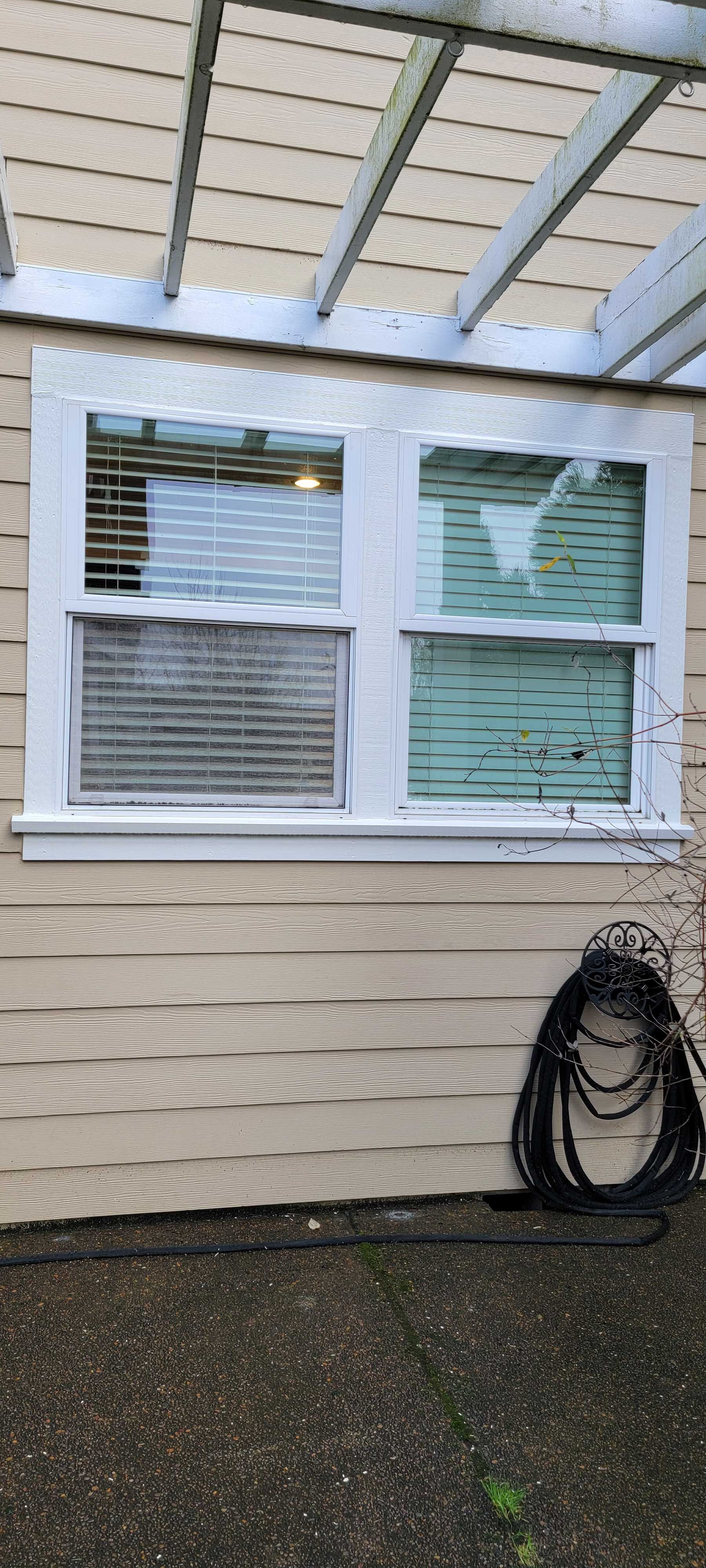 A window with blinds is on a weathered building. A black coil sits below.