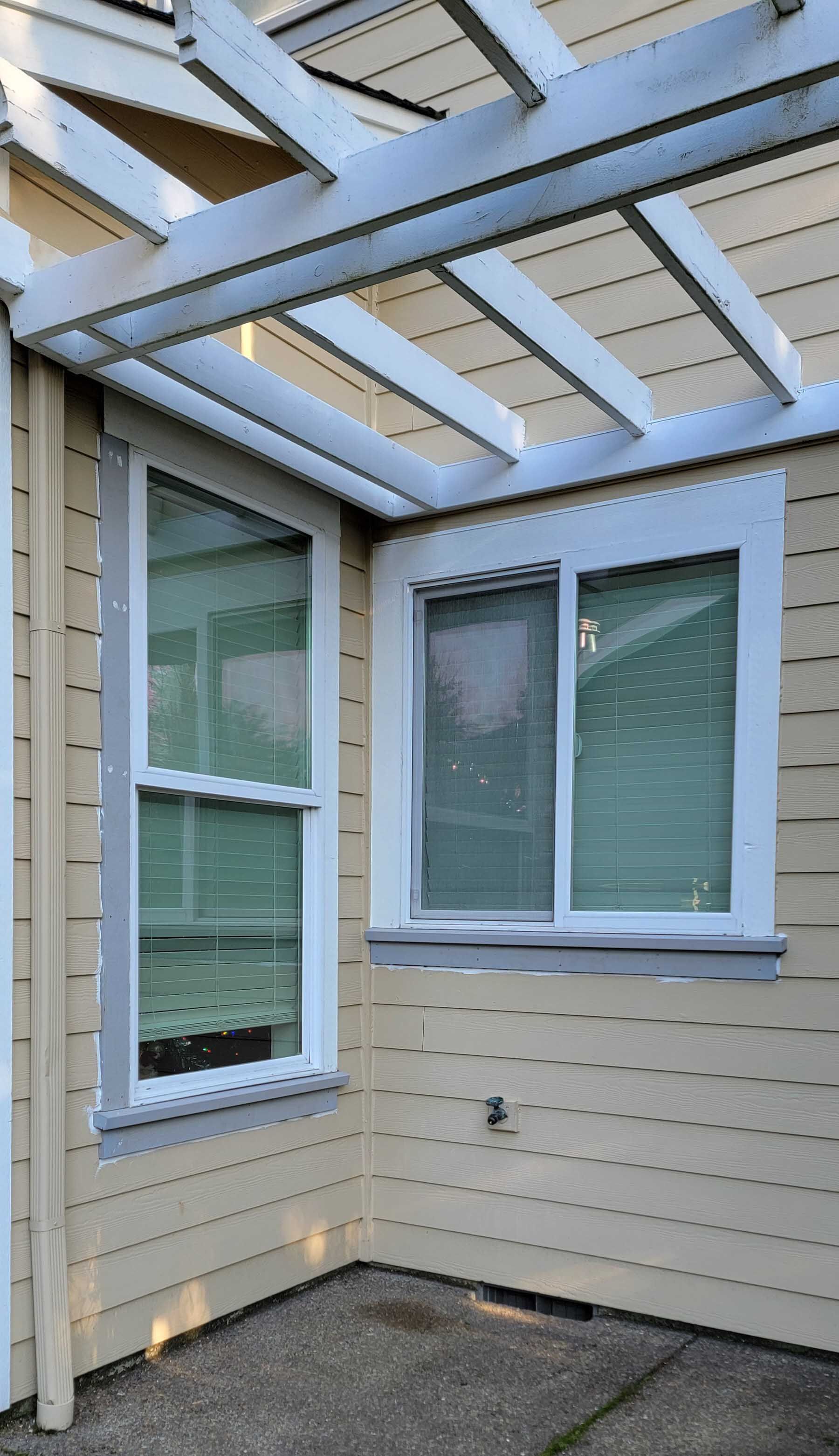 Two windows on a light yellow building, beneath a white pergola. The left window is vertical, the right is horizontal.